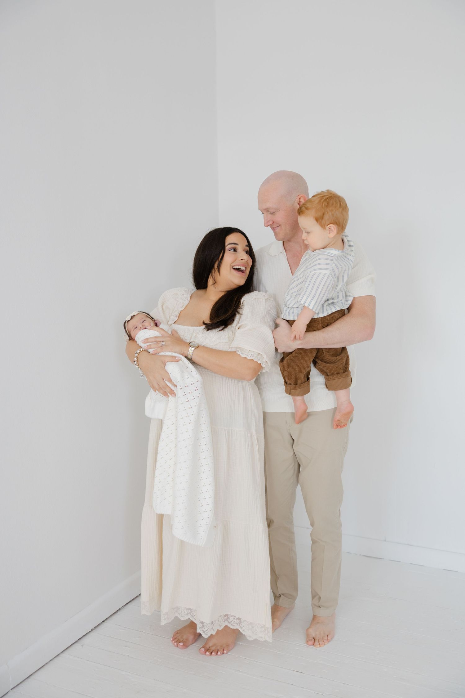 Minimal lifestyle family portrait with parents holding their newborn baby while standing together in a neutral studio setting.