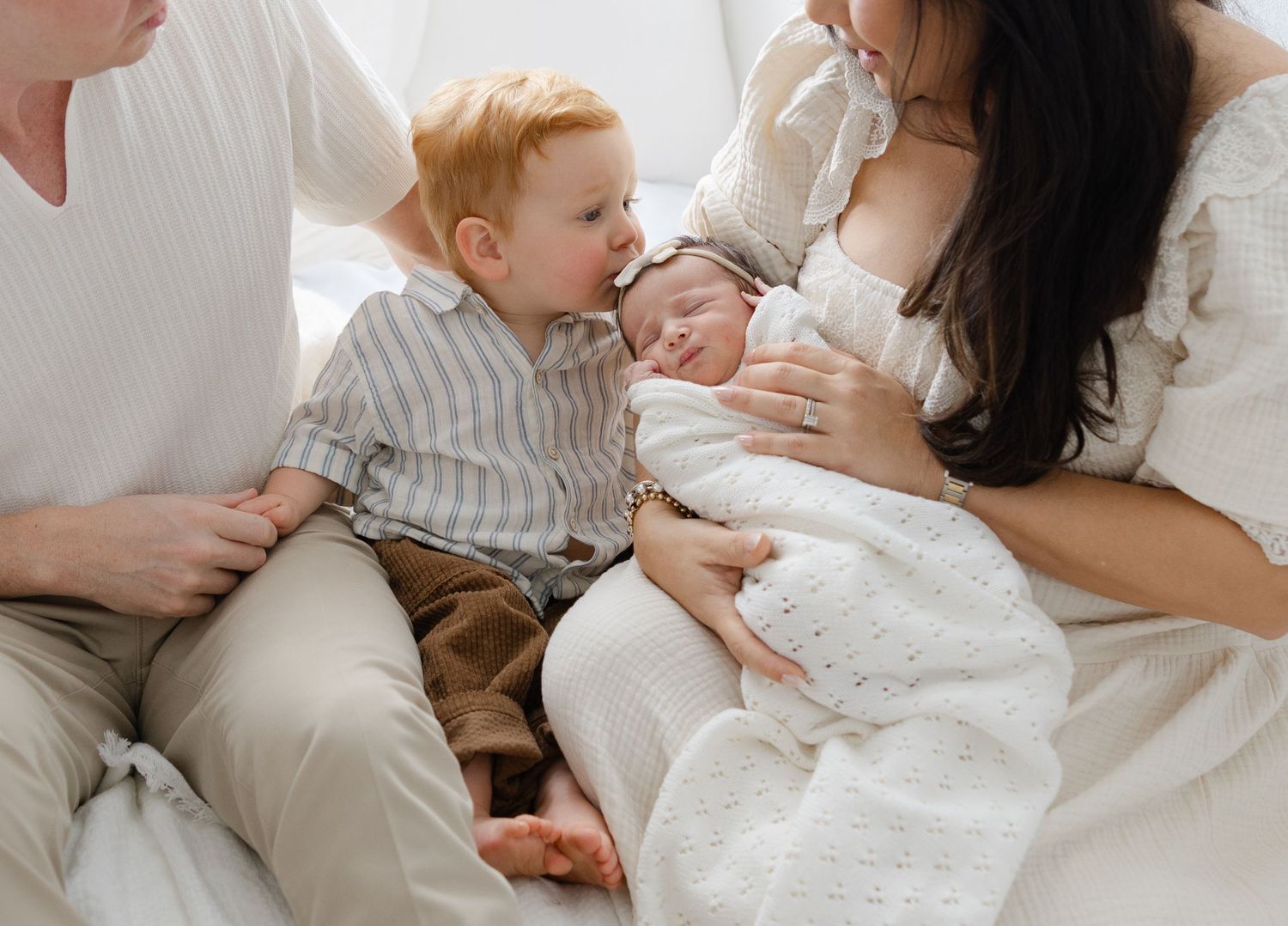 Lifestyle newborn photography session showing parents and a toddler cuddling their newborn baby on a bed in soft natural light.