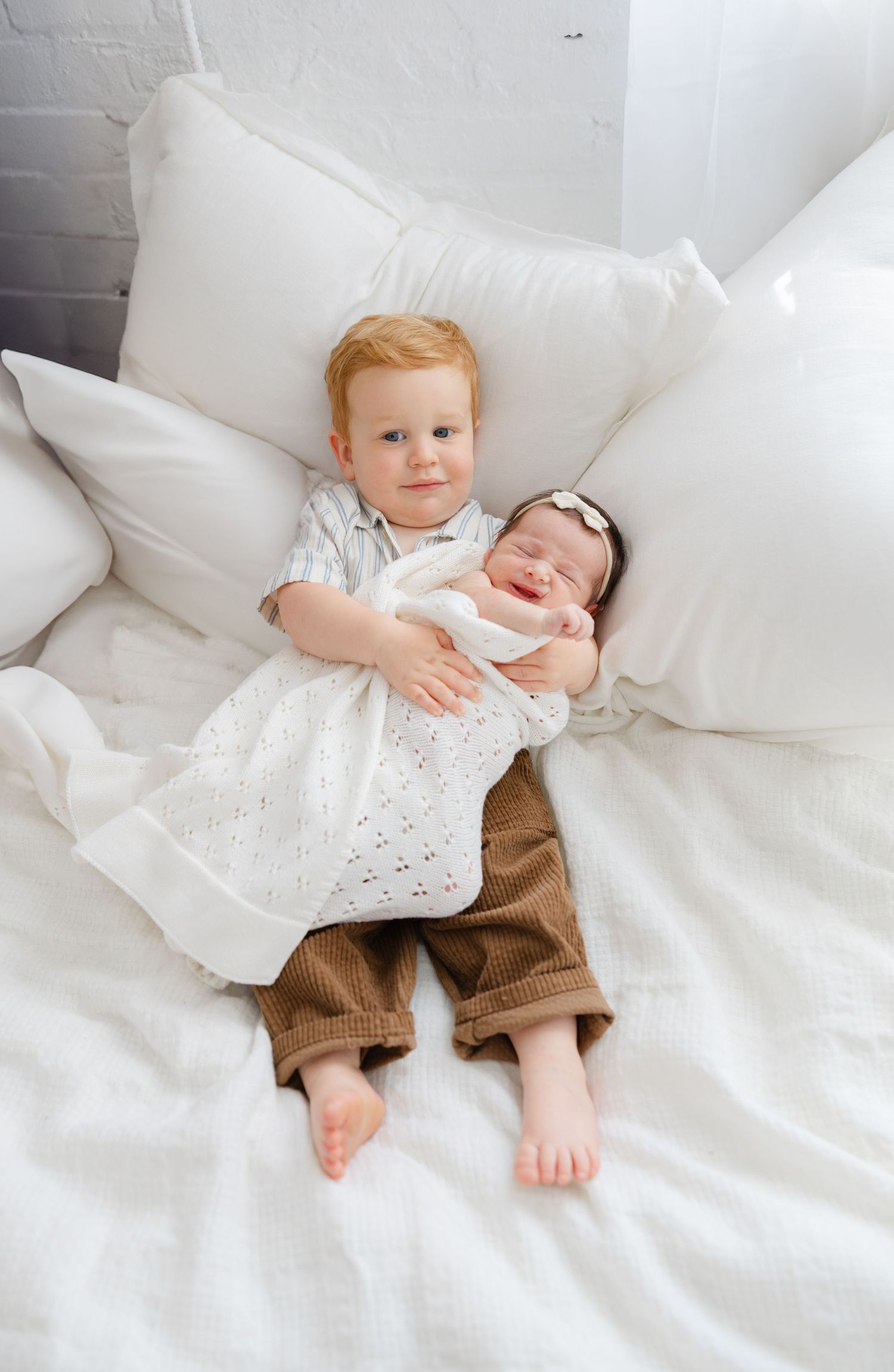 Lifestyle newborn session with parents and toddlers sitting together on a bed while holding their newborn baby.