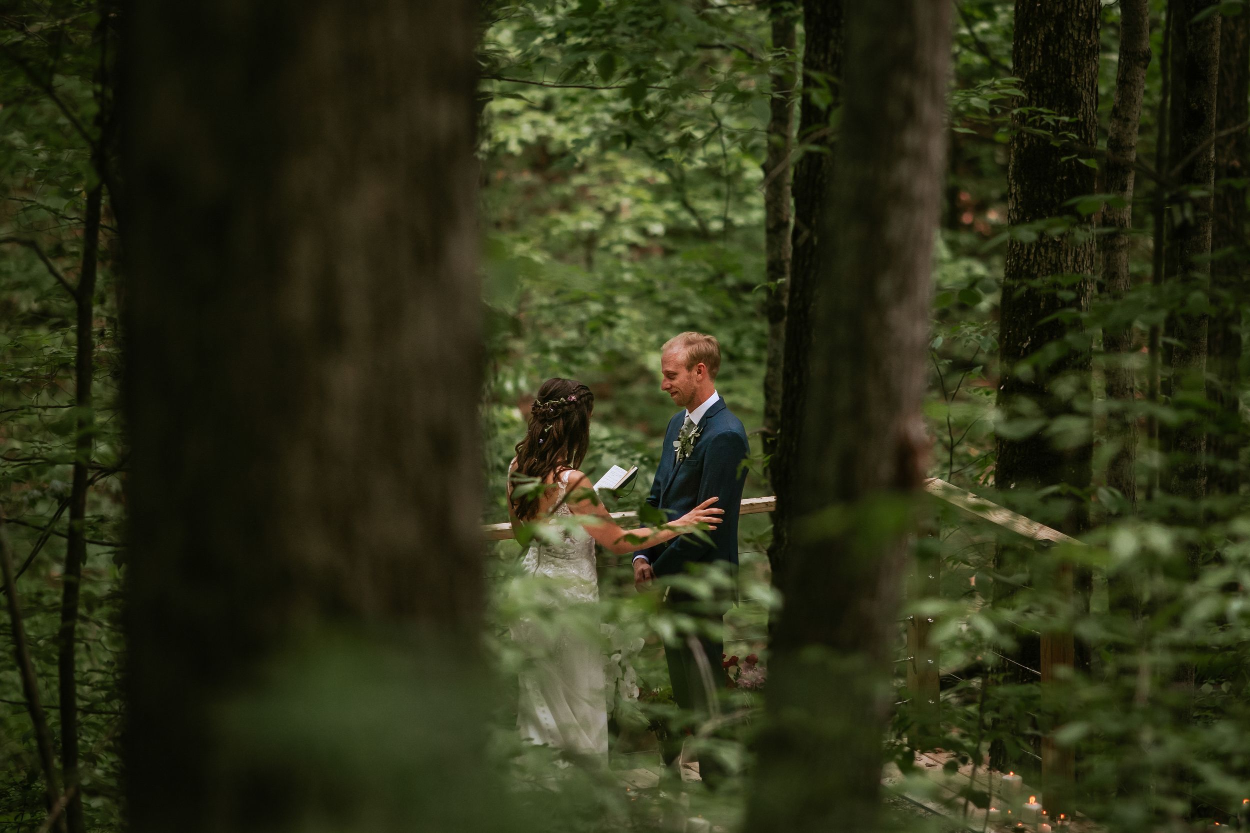 Forest wedding ceremony with rustic wooden seating surrounded by tall trees.