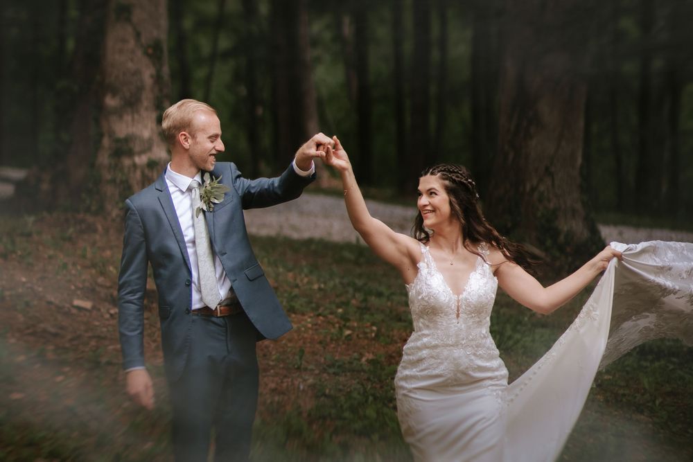 Joyful wedding couple dancing and twirling in a forest setting.