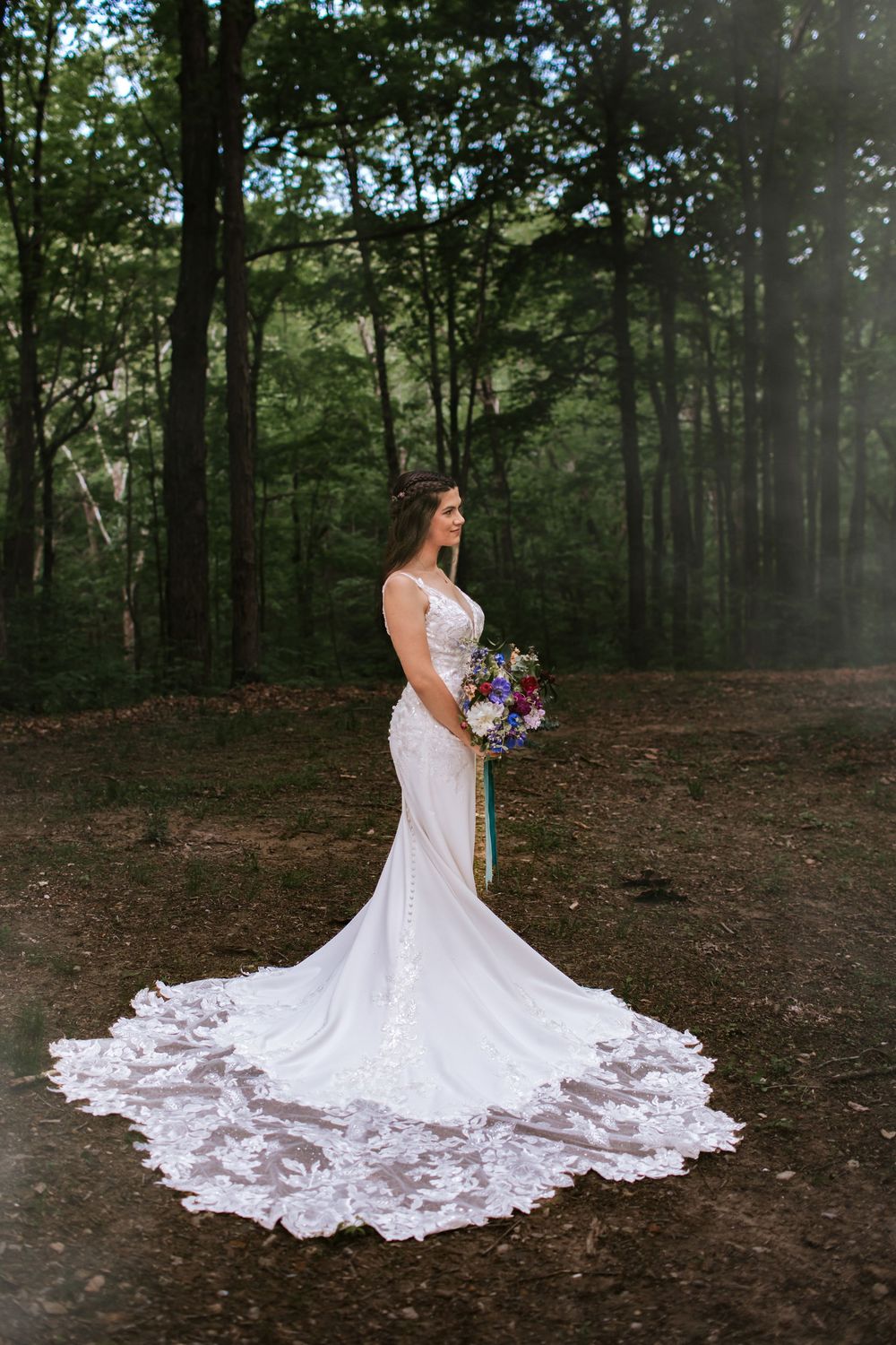 Bride's stunning lace wedding dress with long train spreads beautifully across forest floor.