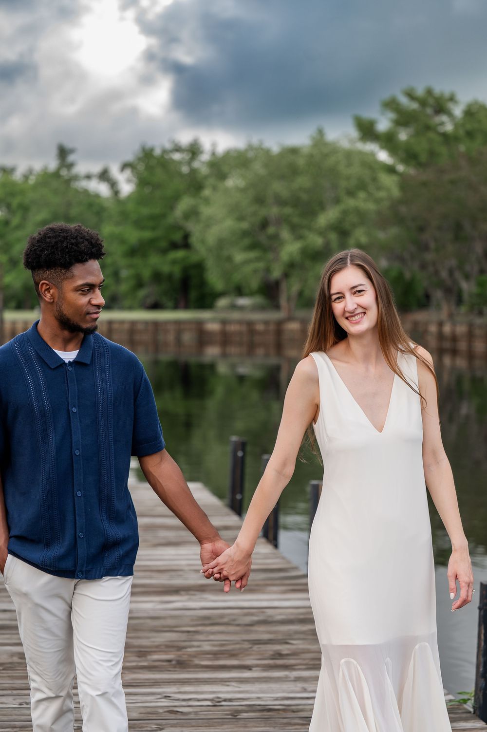 Couple holding hands and walking along a wooden dock by a serene lake.