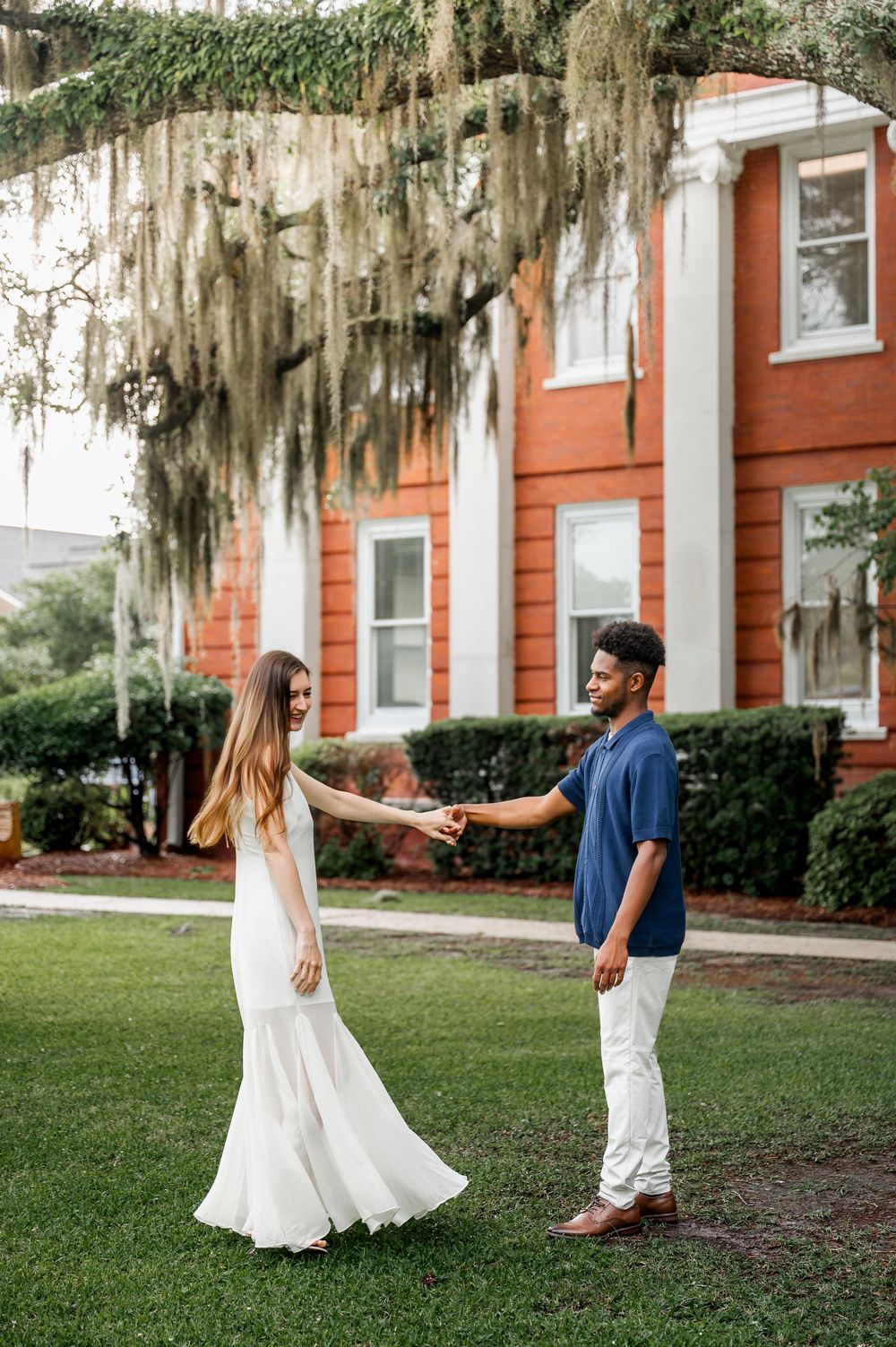 Couple dancing playfully in front of a historic red building with Spanish moss.