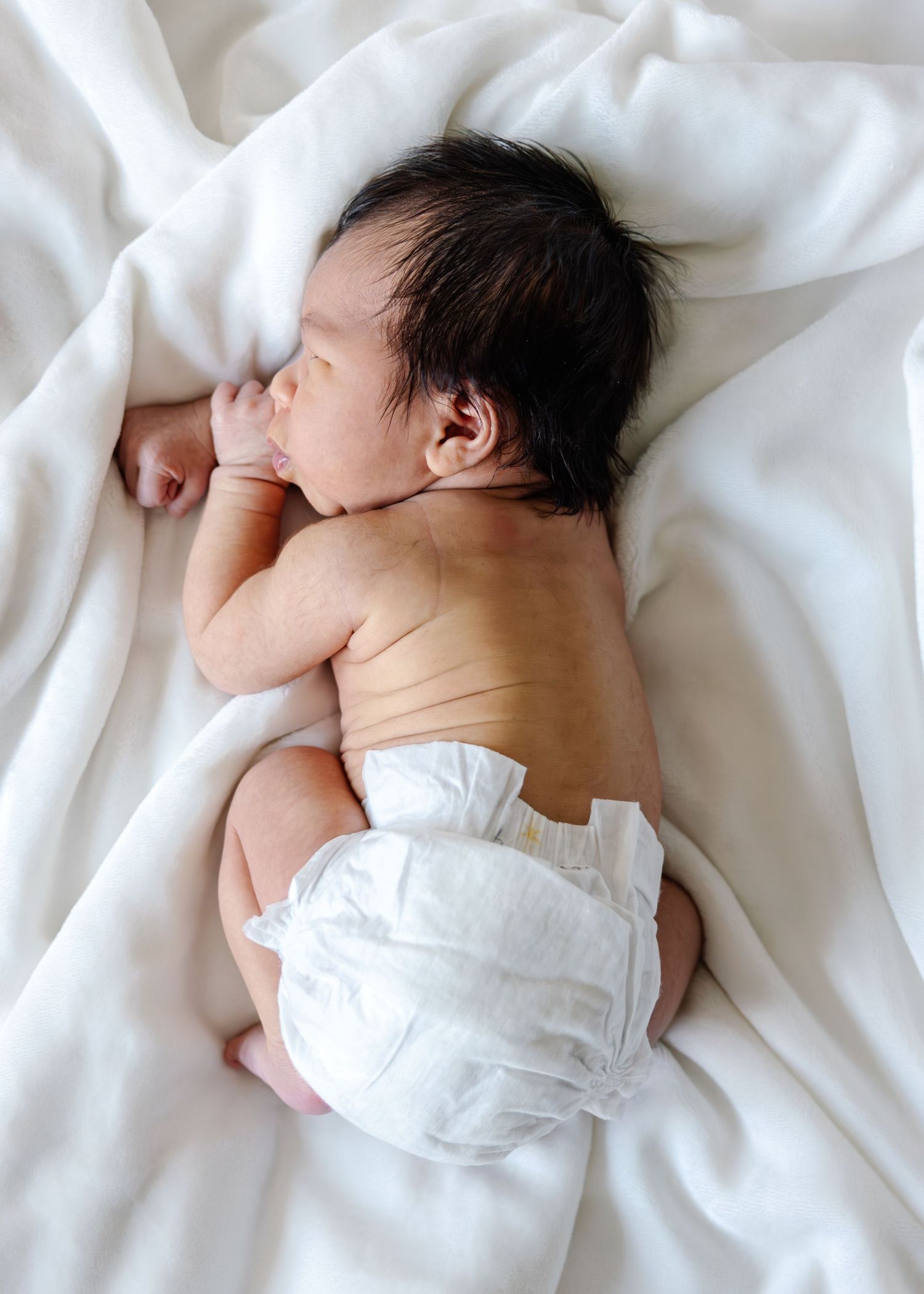 A sleeping newborn baby lies on white bedding in a peaceful pose.