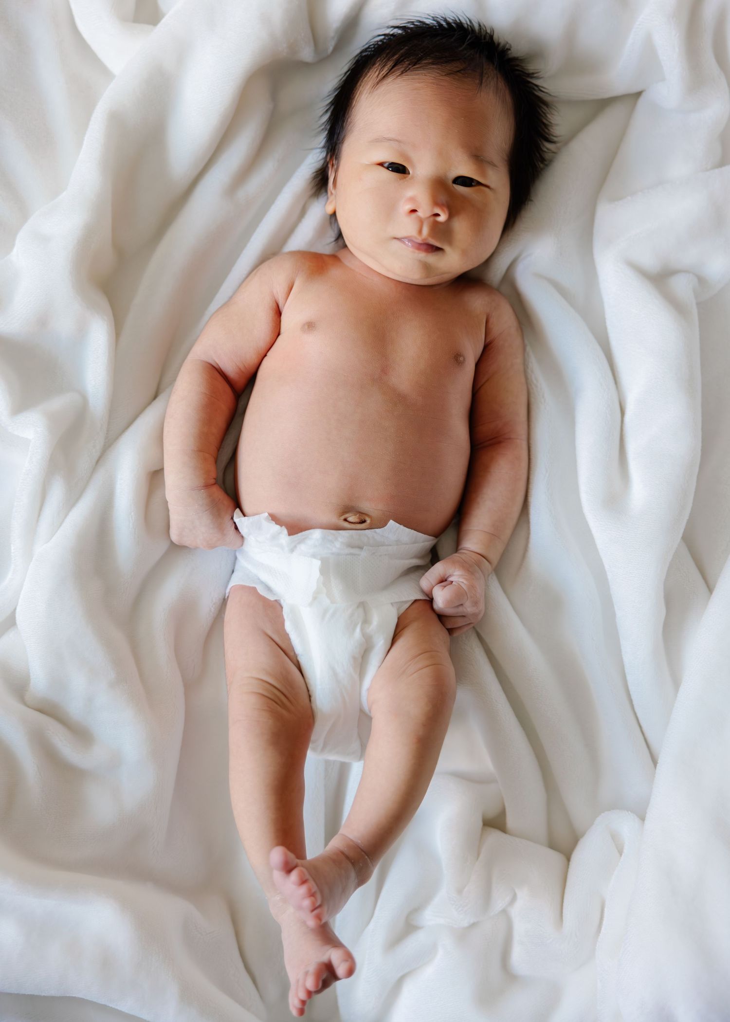 Newborn baby lying on white bedding wearing a diaper in a progression of five similar photos.