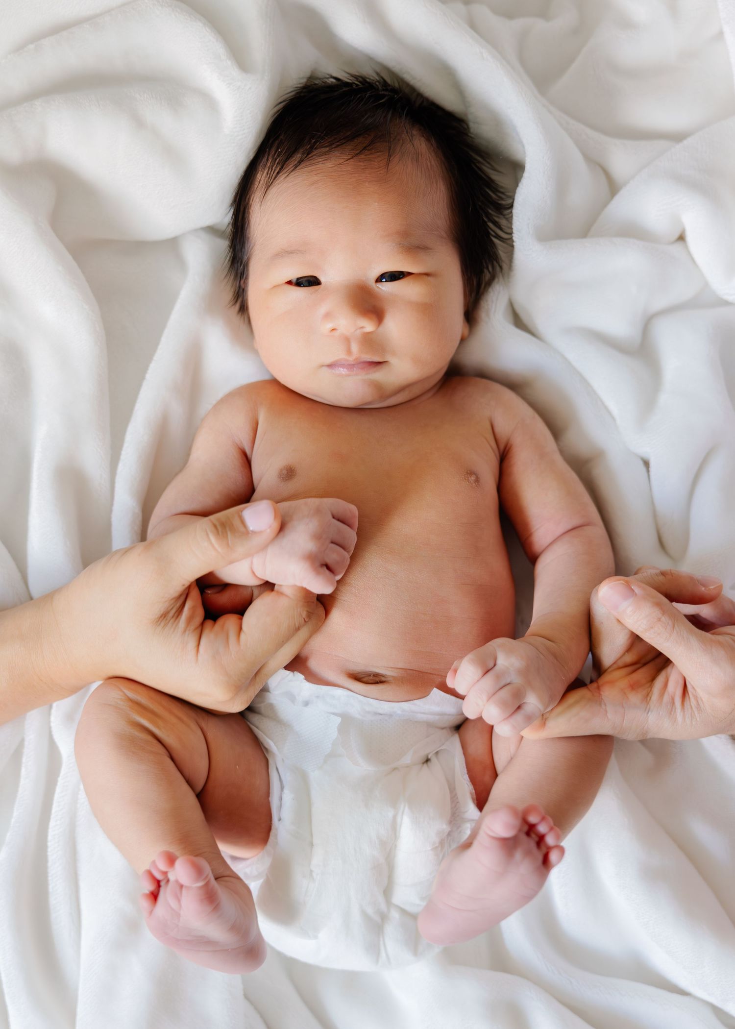 Newborn baby lying on white bedding in a series of gentle poses showing tiny hands and feet.