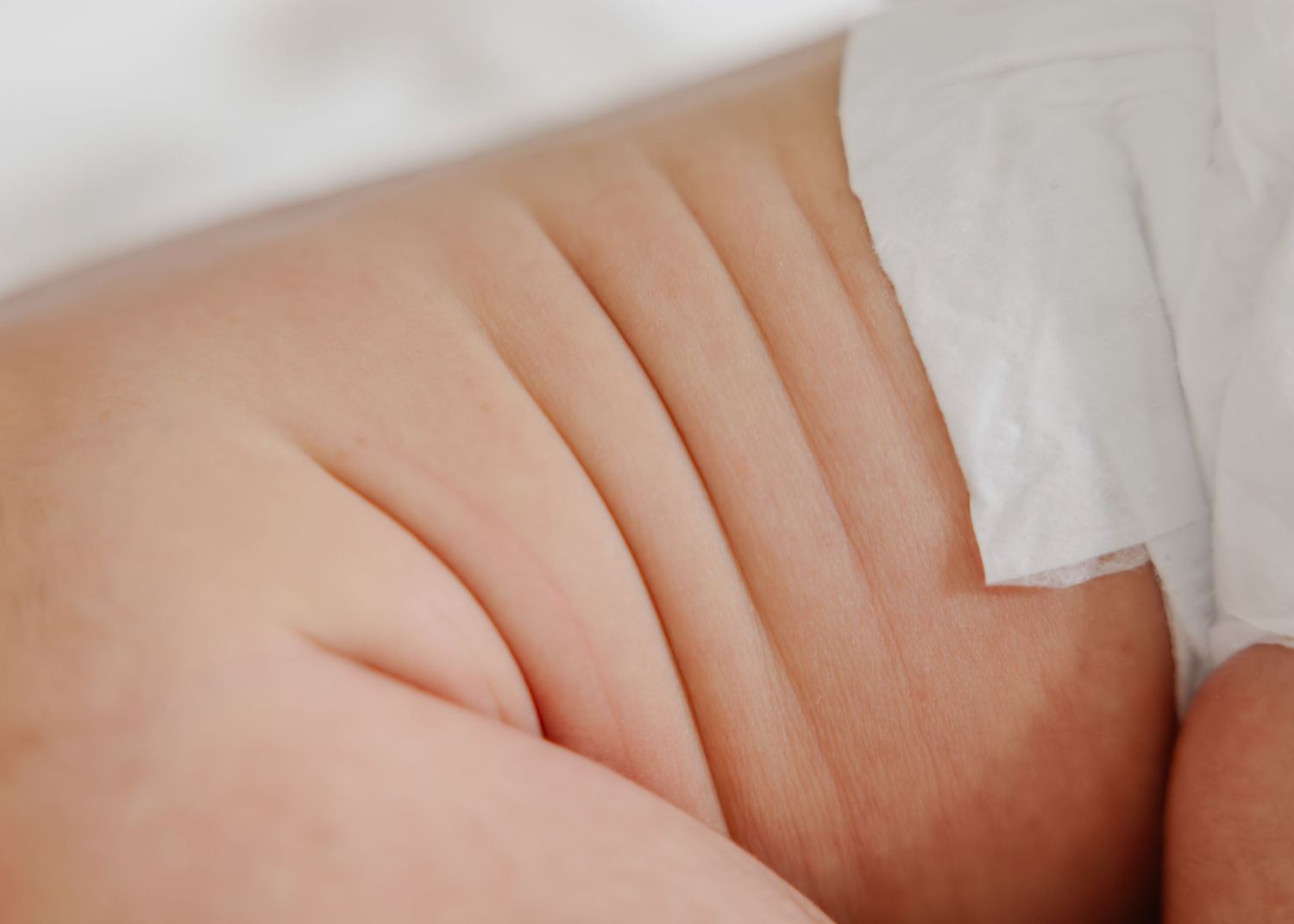 Soft focus image of smooth baby skin with gentle folds and creases against white fabric.