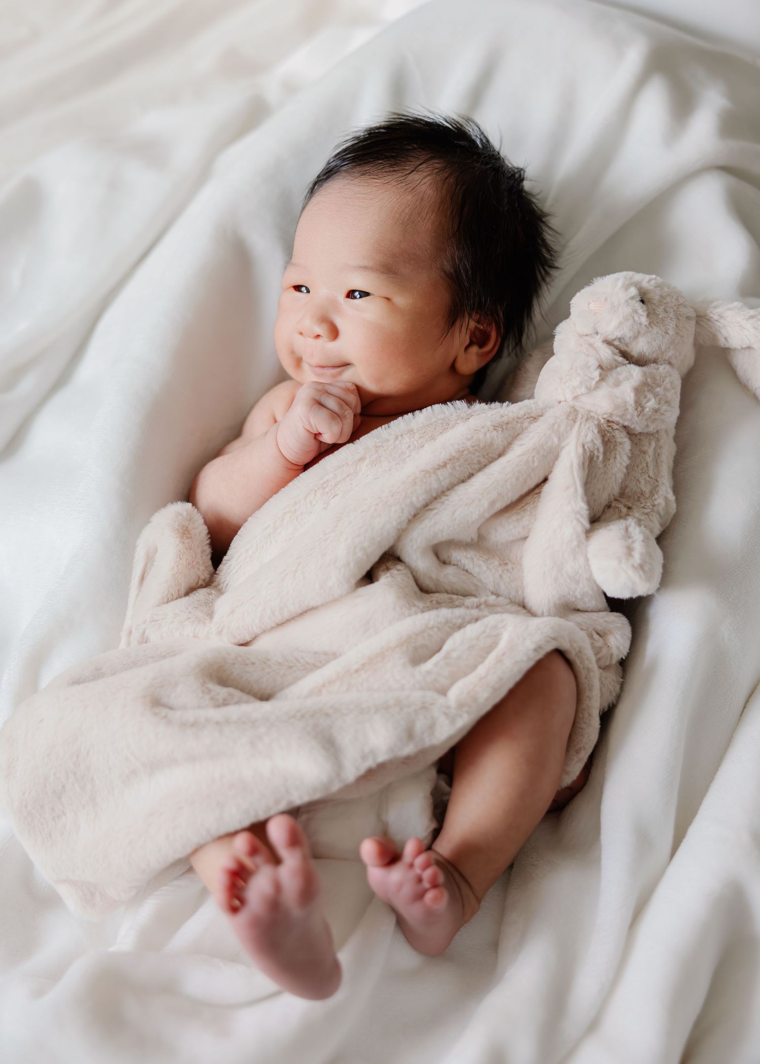 A baby in white blankets lies on white bedding in a series of peaceful sleeping poses.