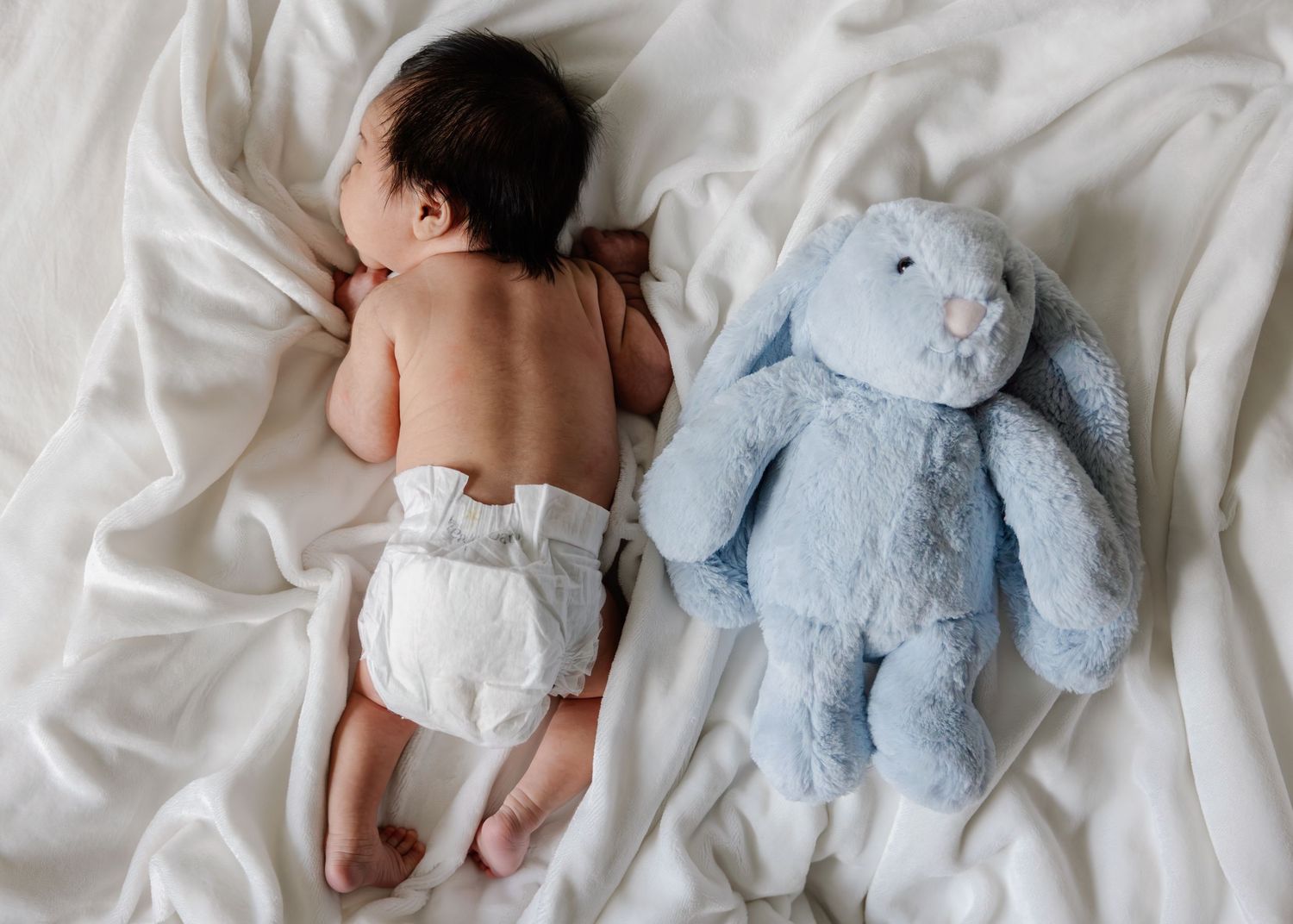 Newborn baby lying on white bedding with blue teddy bear companion in series of connected photos.
