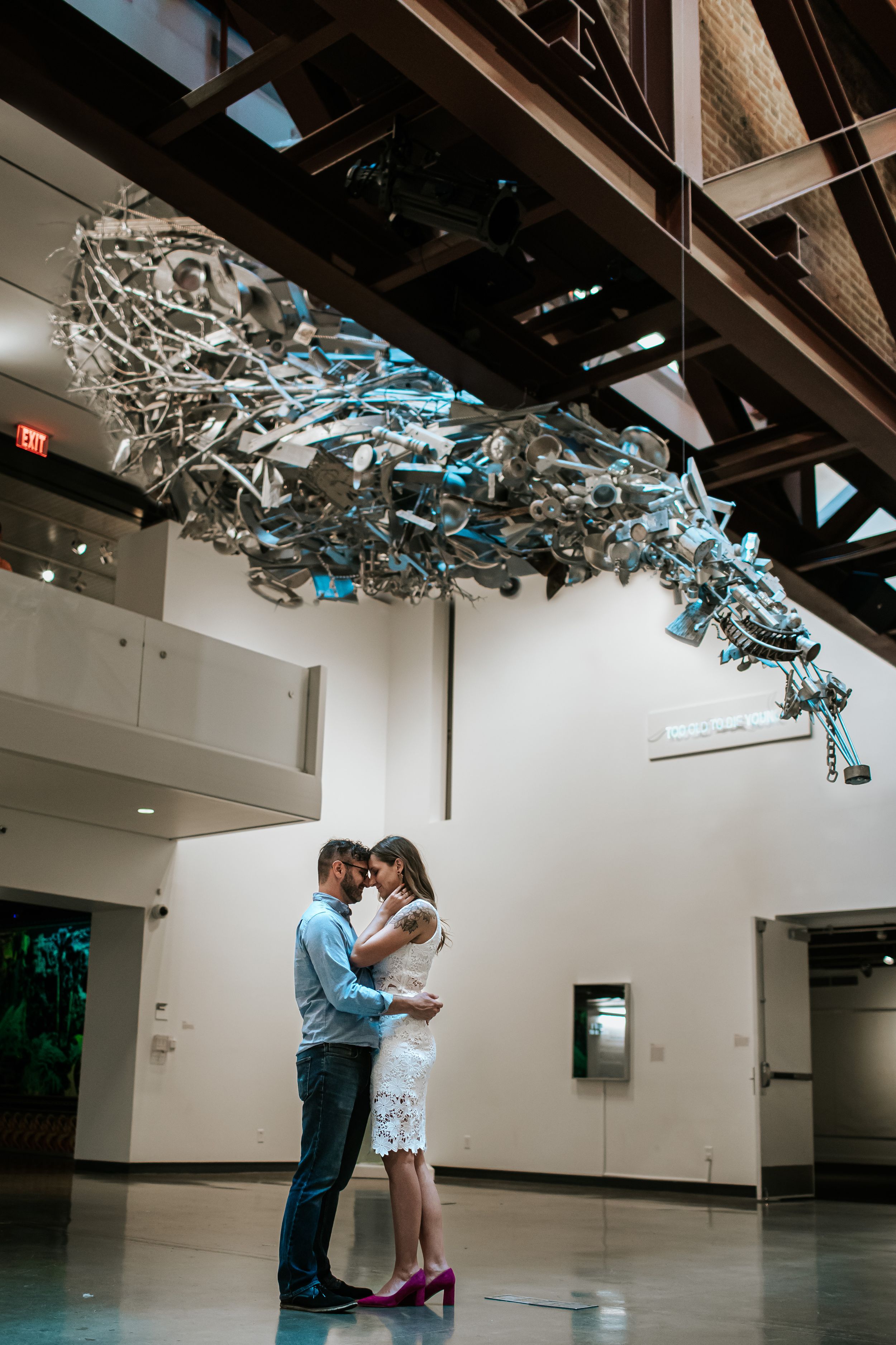 Couple dancing in a modern gallery space with metallic ceiling sculptures and white walls.