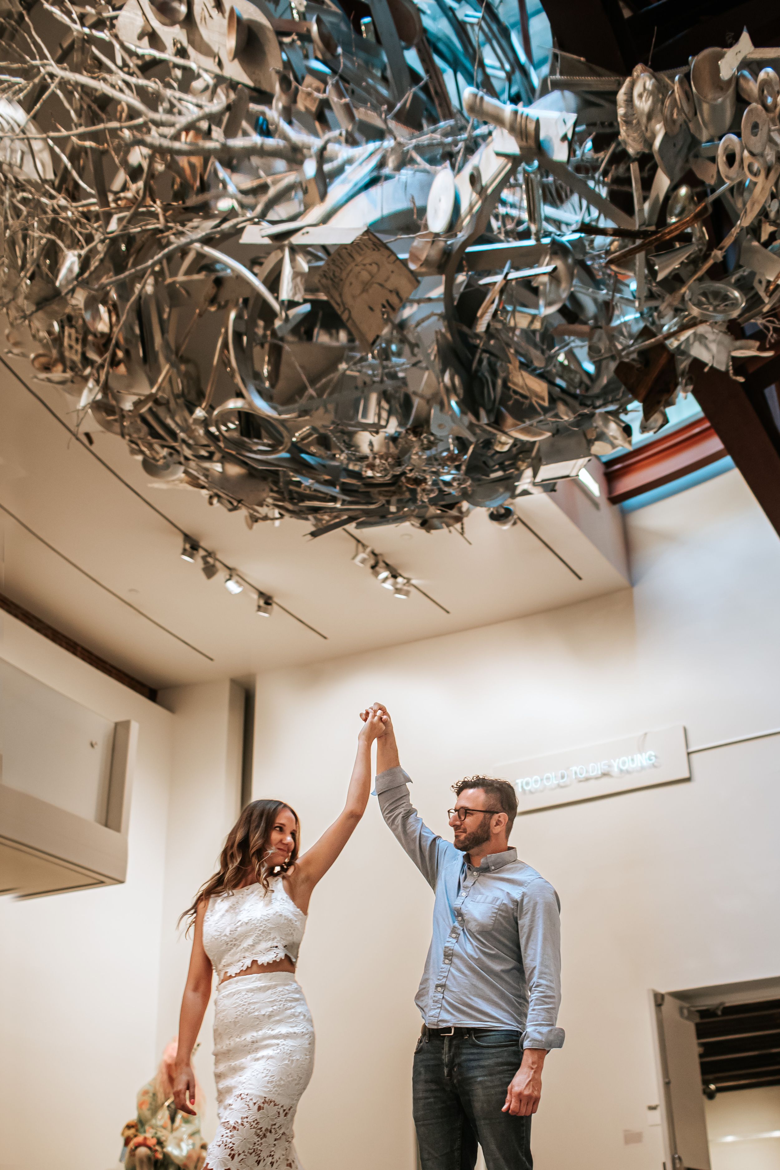 A couple dances playfully under a silver metallic ceiling decoration in a white room.