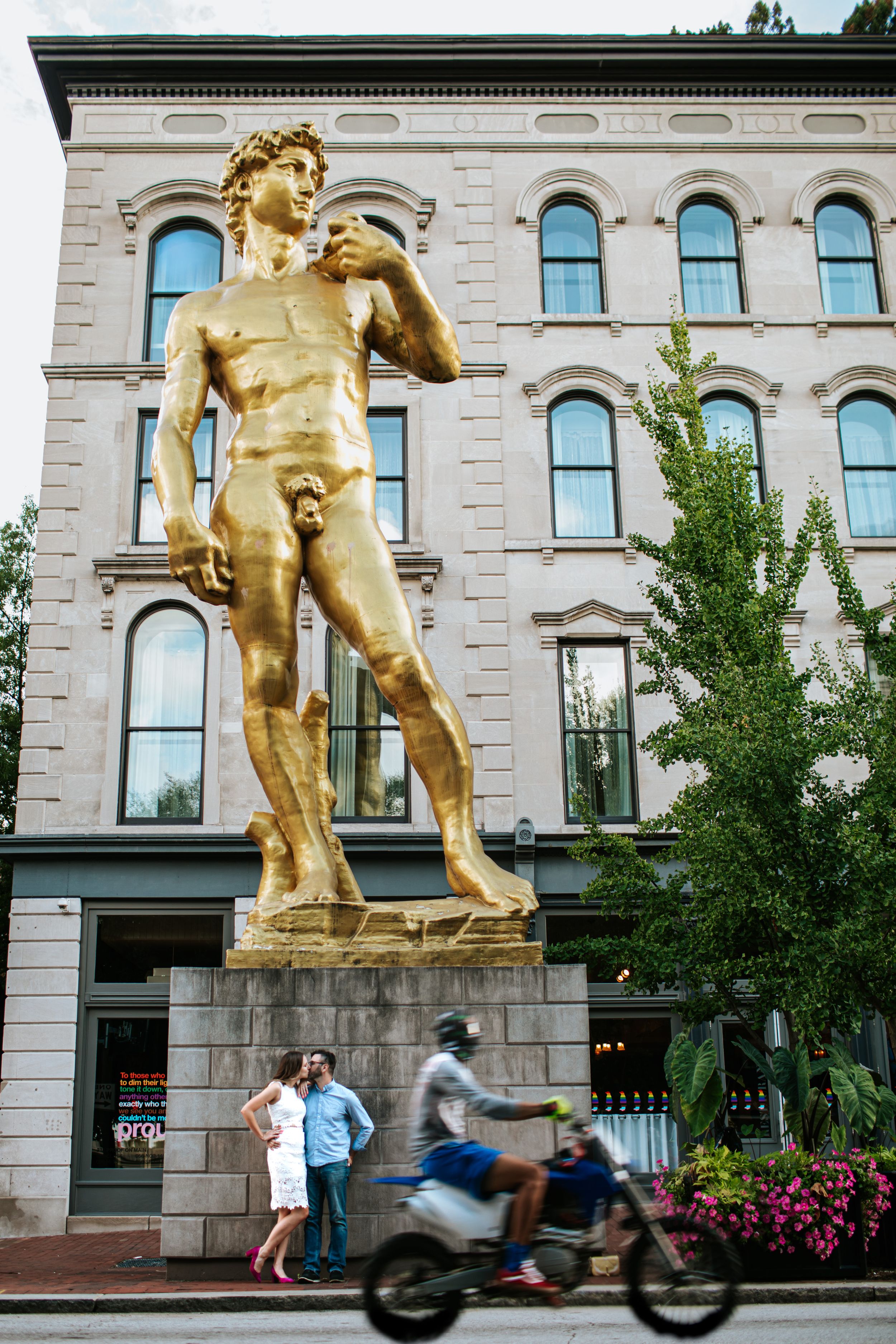 A golden statue stands prominently in front of a classical stone building with arched windows.