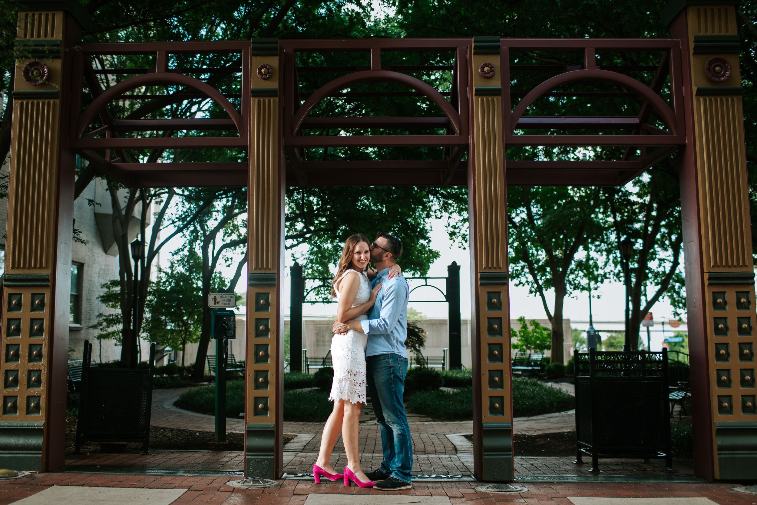 Romantic couple shares intimate moments under an ornate gazebo surrounded by lush greenery.