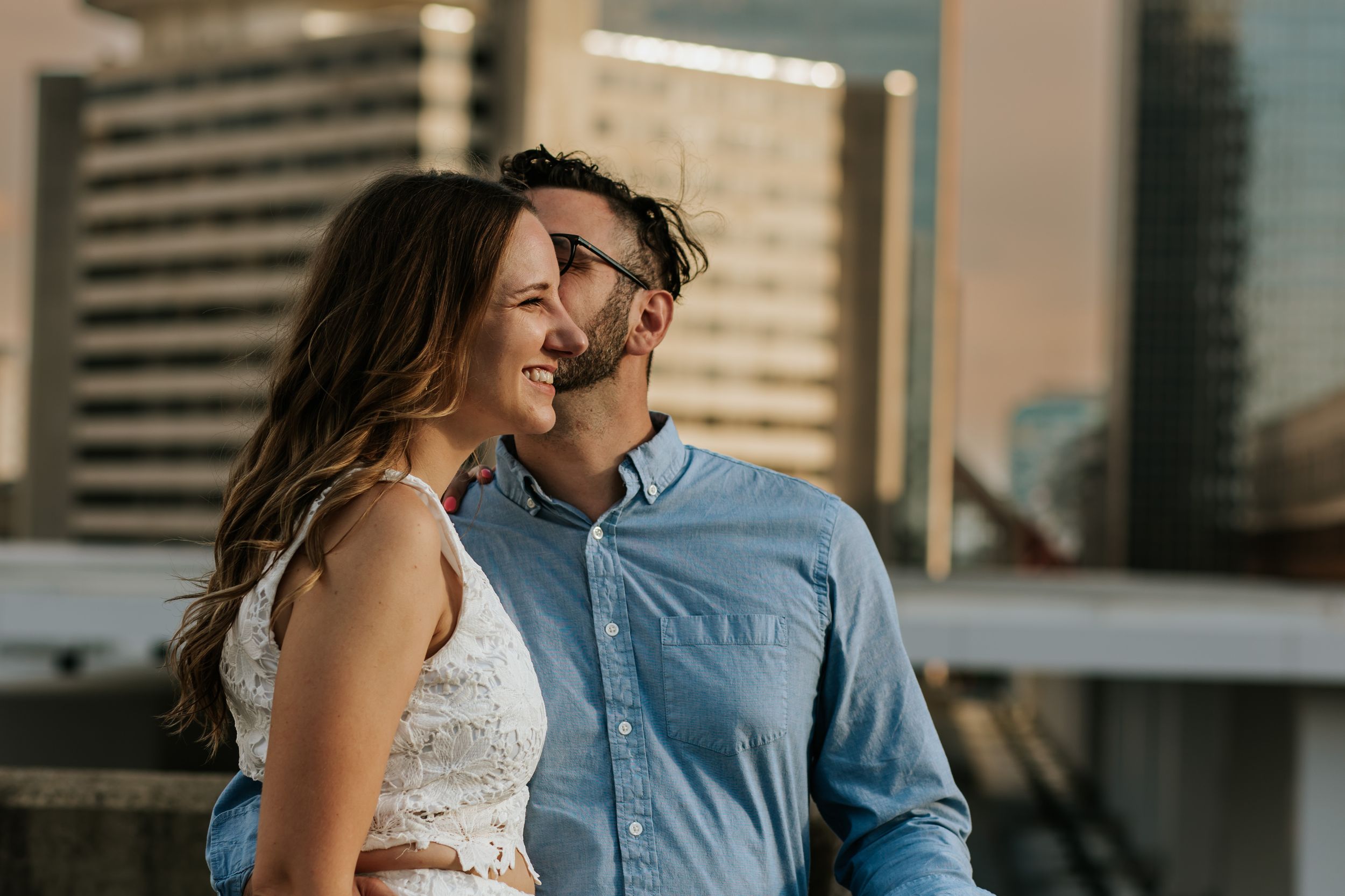 Couple in casual attire sharing tender moments against urban backdrop with tall buildings.