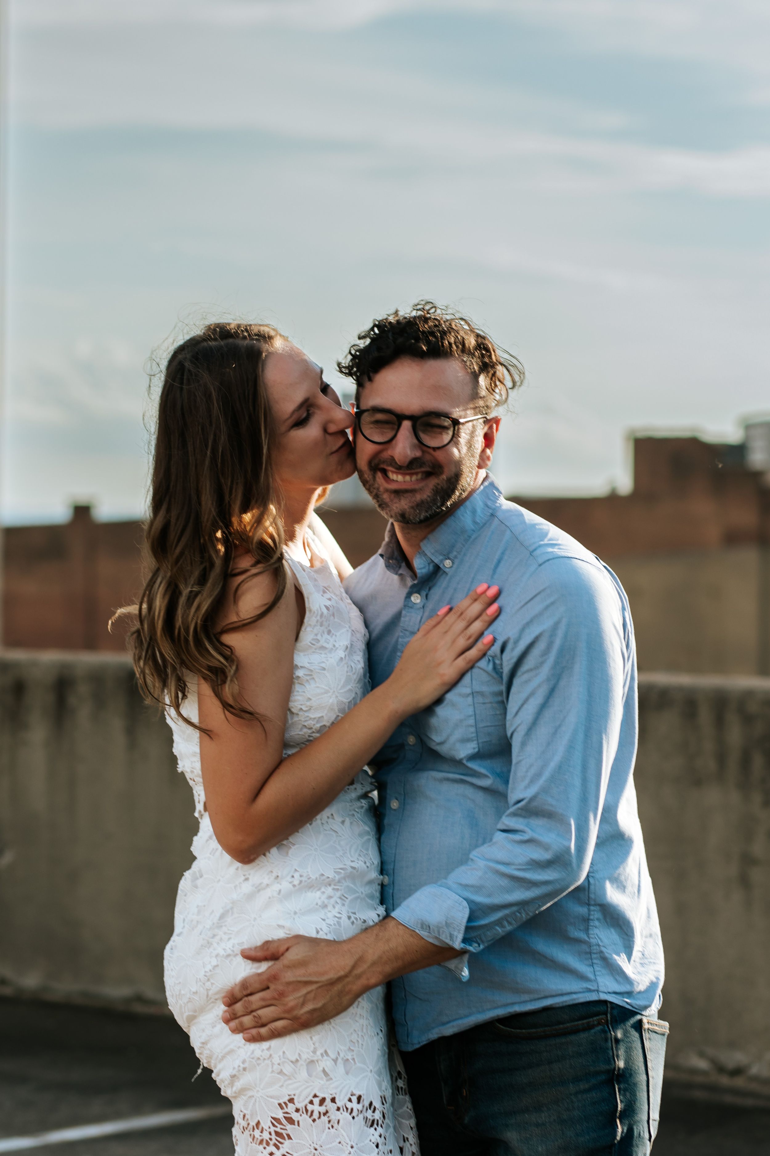 A couple shares an intimate moment on a rooftop against a cloudy sky.