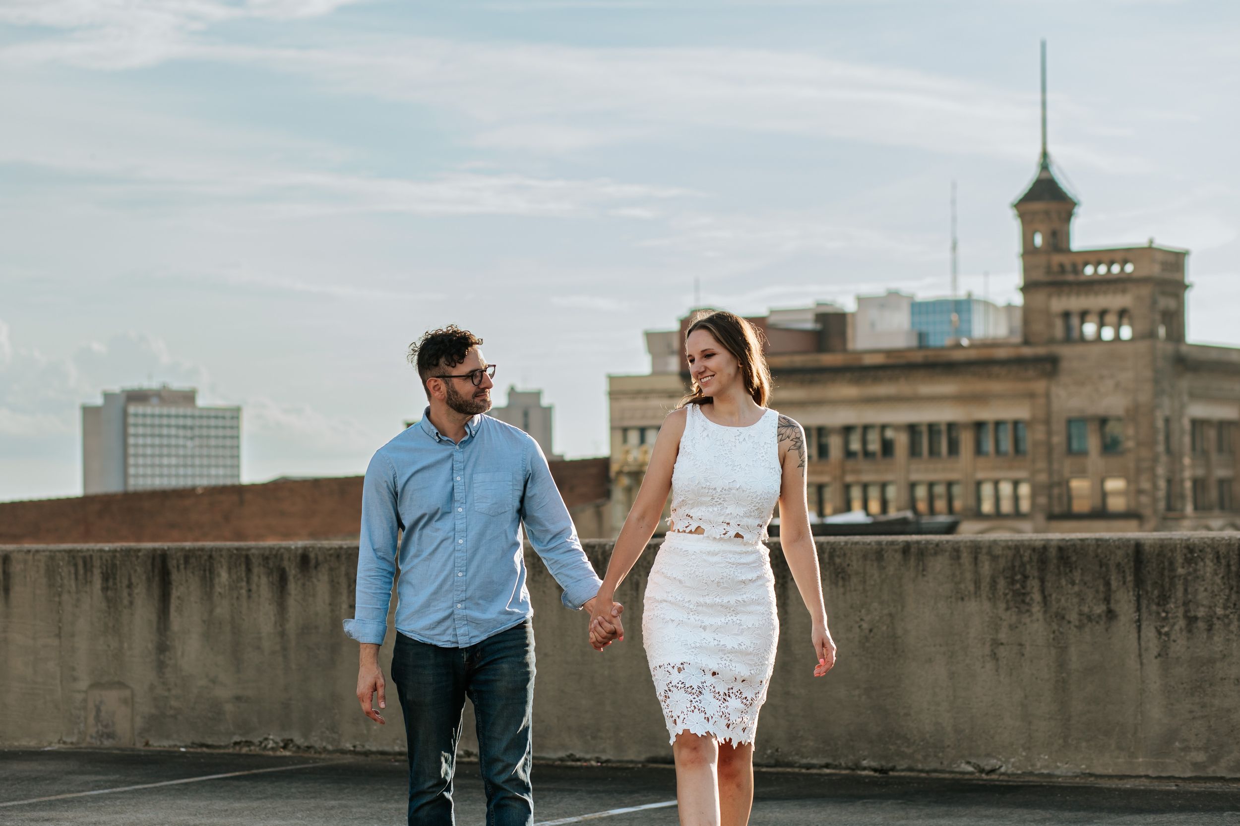 A couple in casual attire walks together and laughs while strolling along an urban sidewalk.