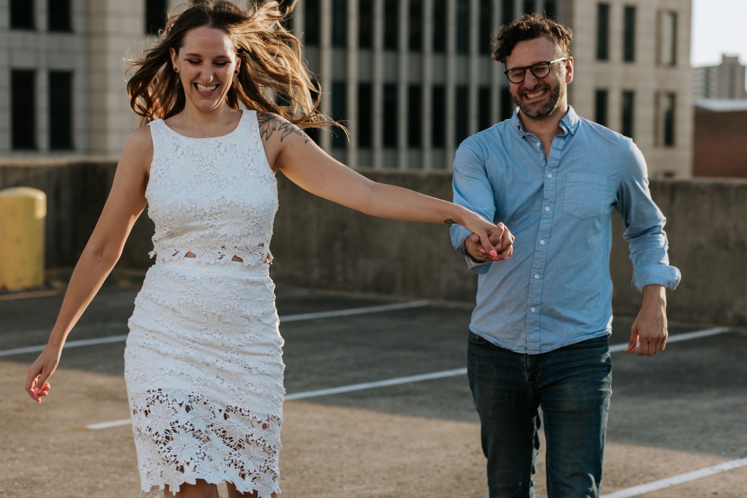 Playful couple running and laughing together along an urban sidewalk.