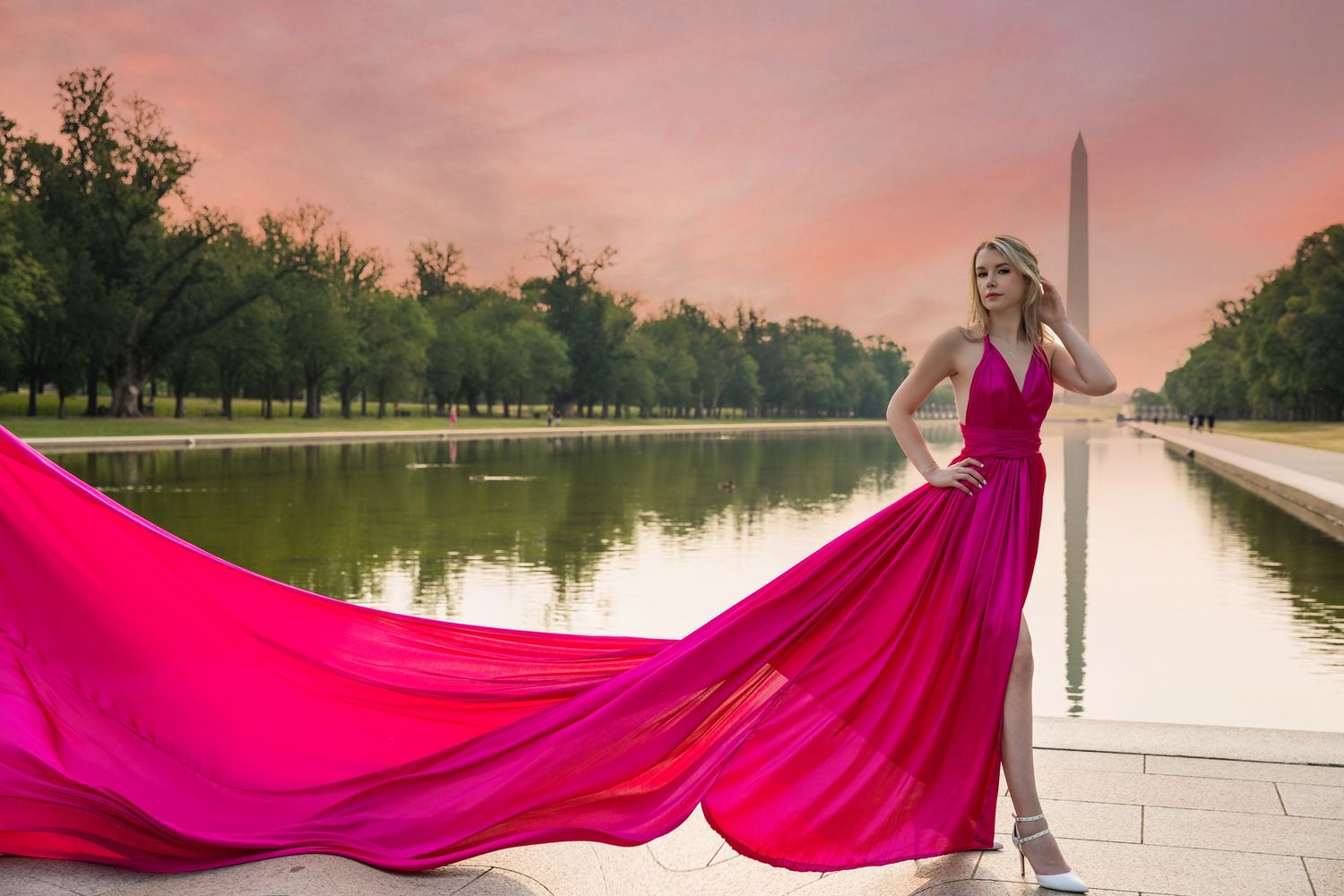 A person in a flowing magenta gown poses dramatically against a sunset backdrop near a reflecting pool. Flying Dress Photoshoot