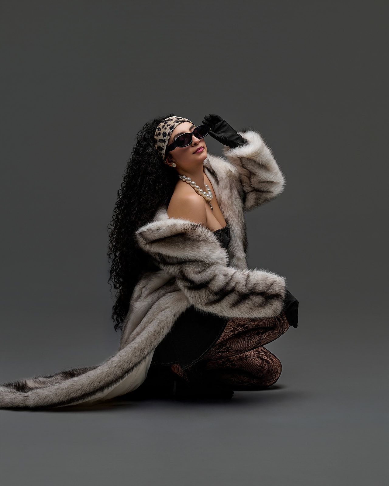 A figure in a beige fur coat poses dramatically against a dark backdrop in an artistic fashion series.