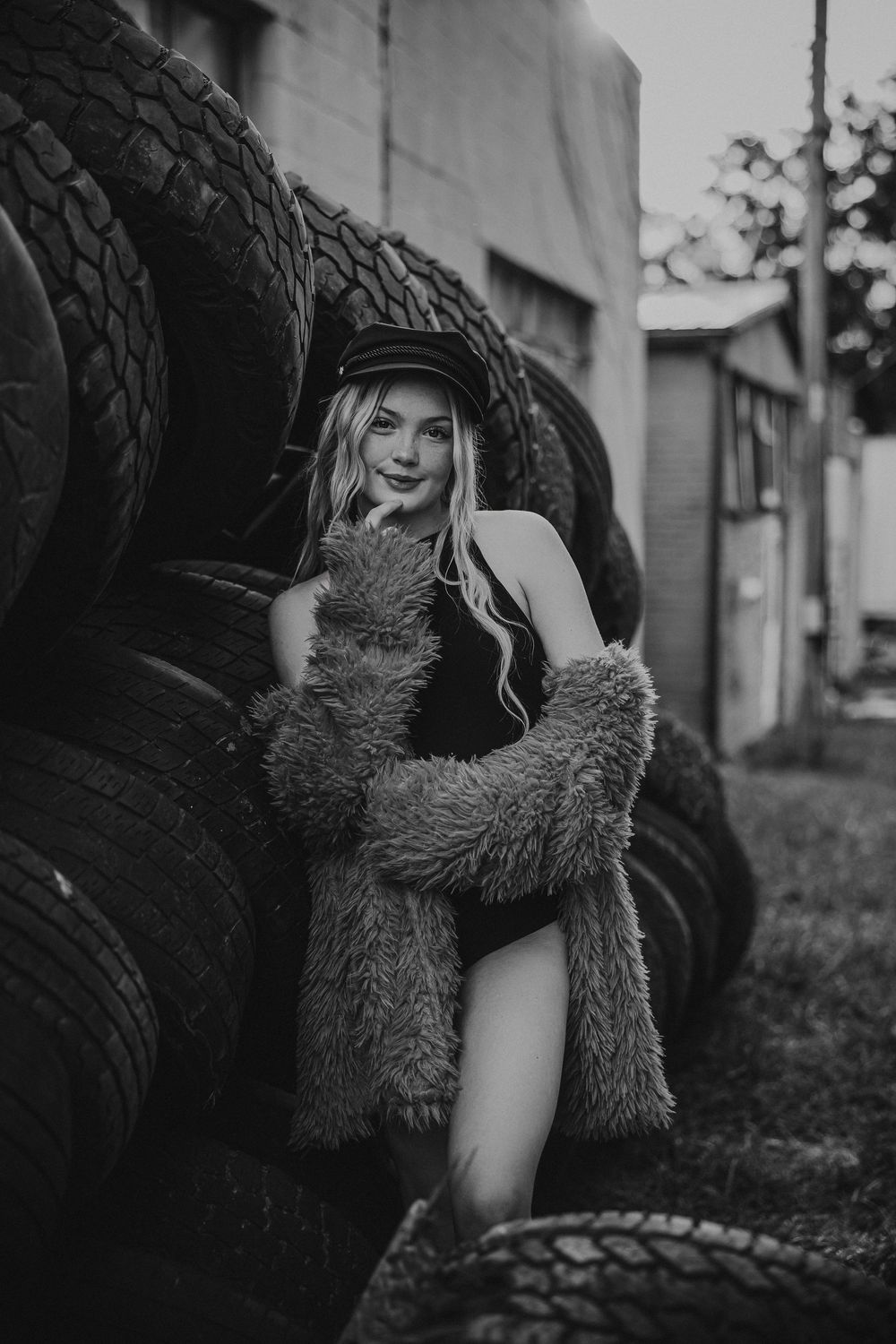 A person in a furry coat and cap poses artistically against a dark background in a black and white photo series.