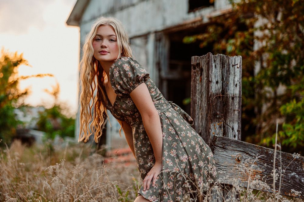 Artistic outdoor photography session among tall grass and wooden posts at golden hour.