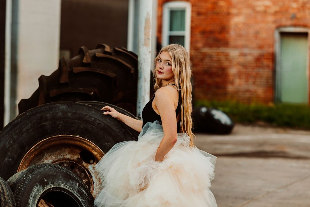 A woman in a white dress poses against rustic brick walls and doorways in an outdoor photo session.