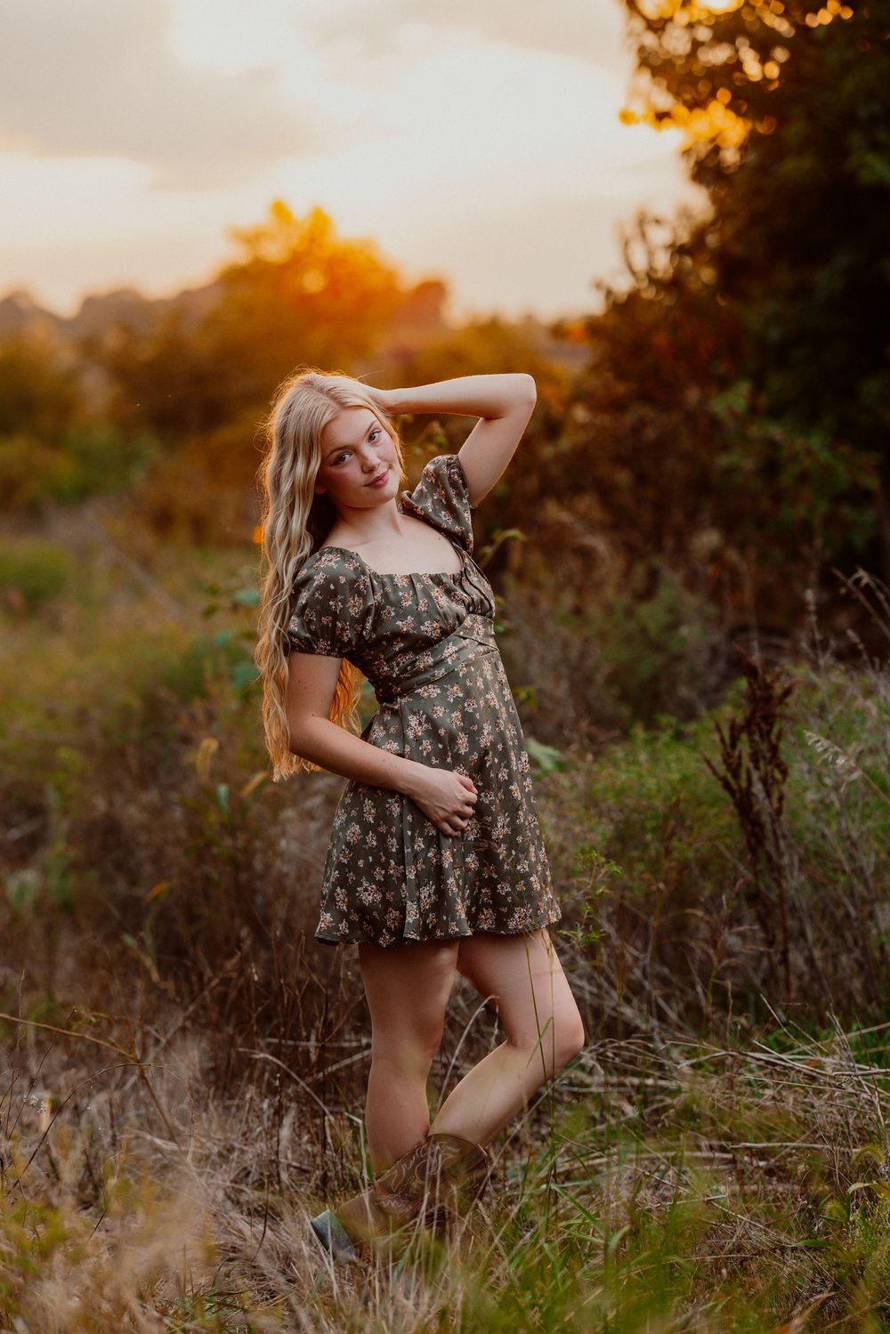 Artistic outdoor boudoir photoshoot in a field at golden hour with warm sunset lighting and natural foliage.