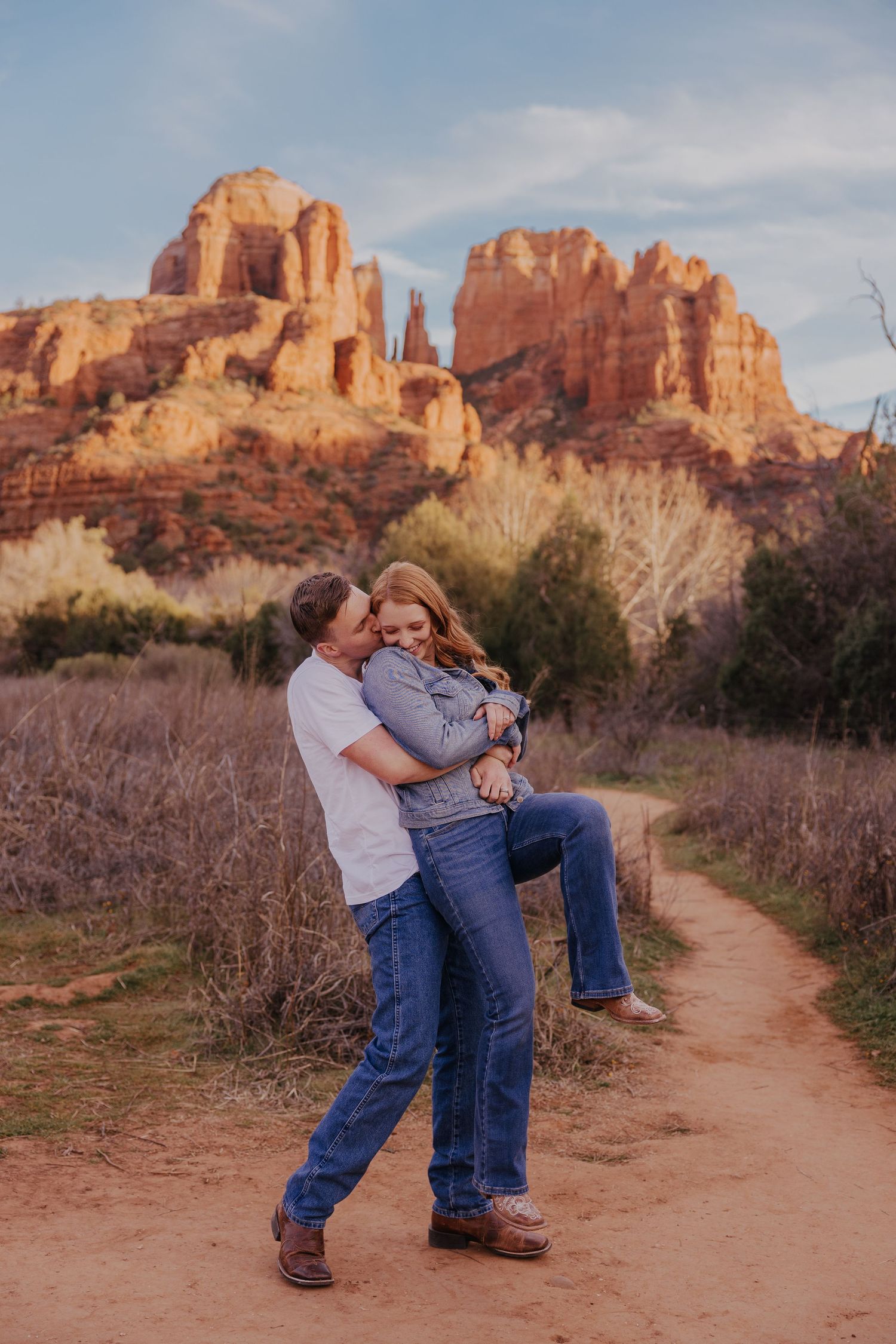 Couple embracing on a desert trail with stunning red rock formations of Sedona in the background.