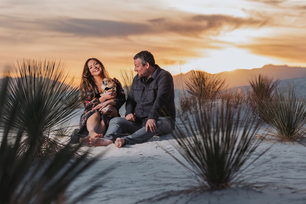 A couple shares an intimate moment against a dramatic desert sunset with yucca plants in the foreground.