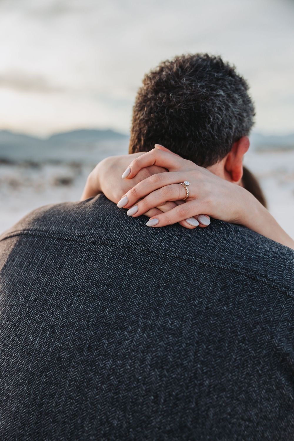 Close-up view of hands gently resting on shoulders wearing a dark sweater against a blurred background.