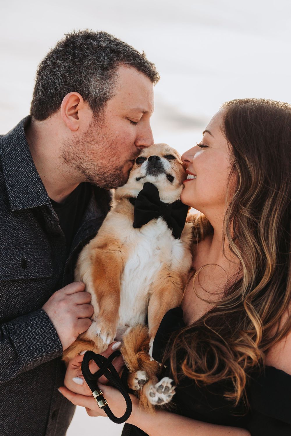 A couple shares a sweet moment kissing their dog who is cradled between them.
