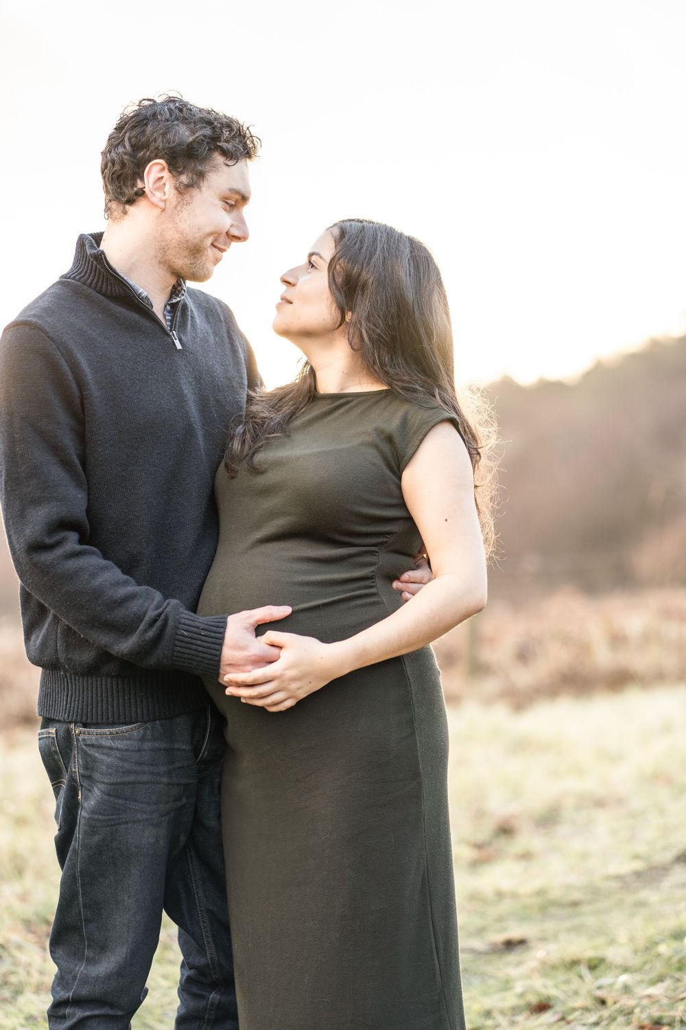 Couple embraces in a romantic outdoor photoshoot at sunset in a grassy field.