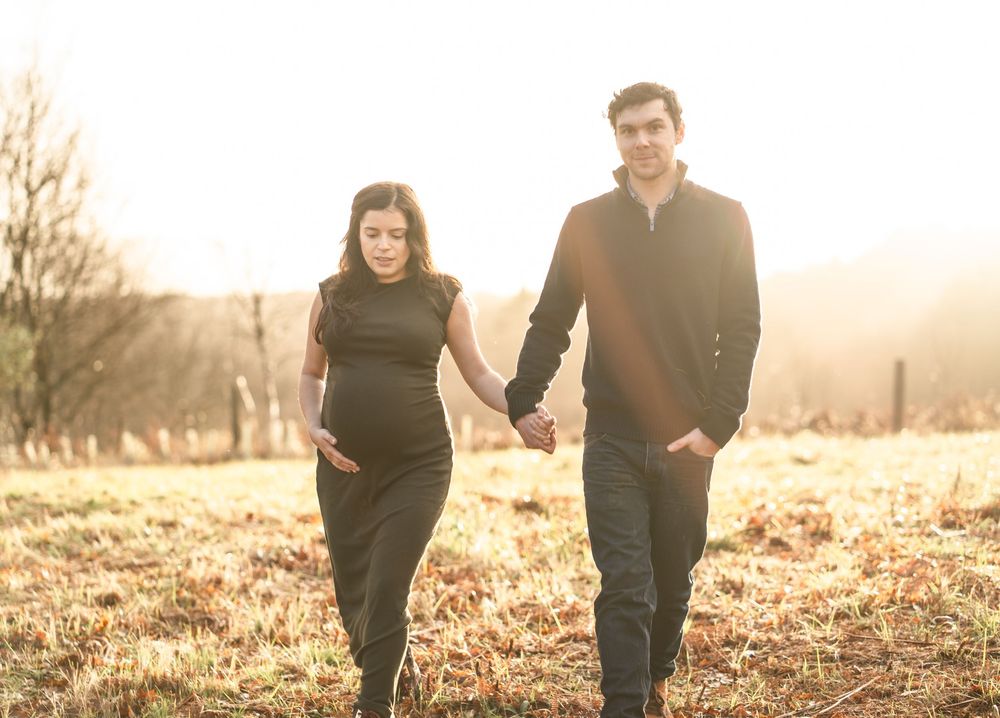 Couple walks hand in hand through a golden field during sunset photography session.
