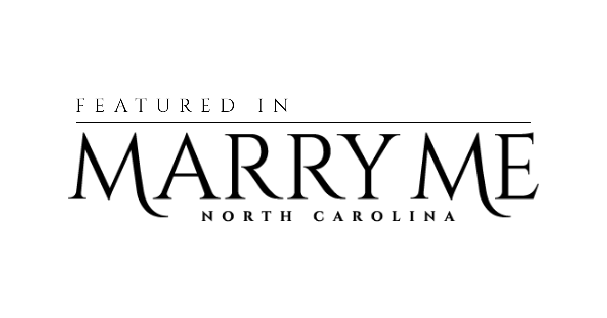 A rustic wooden sign with 'Marry Me North Carolina' text and floral decorations in a romantic outdoor setting.