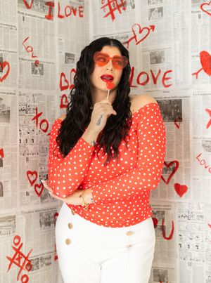 A red polka dot dress against a backdrop of newspaper pages decorated with red hearts and love doodles.