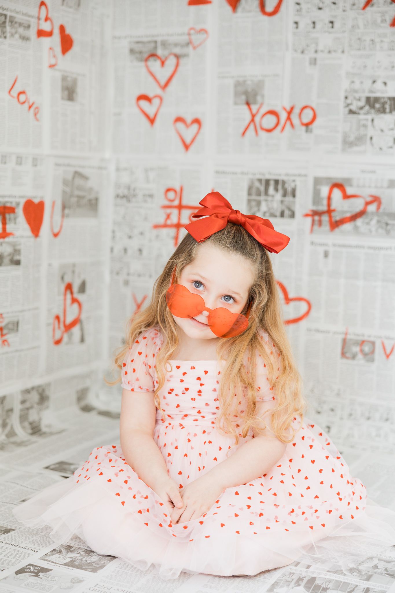 A white and red heart-themed Valentine's Day photo setup with newspaper backdrop and romantic decorations.
