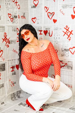 Red polka dot top and white pants outfit against newspaper wall decorated with red hearts and doodles.