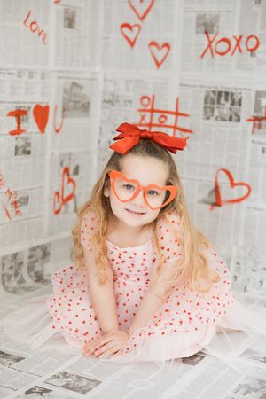 A whimsical portrait on newspaper backdrop with orange bow and glasses, featuring polka dot dress and playful poses.