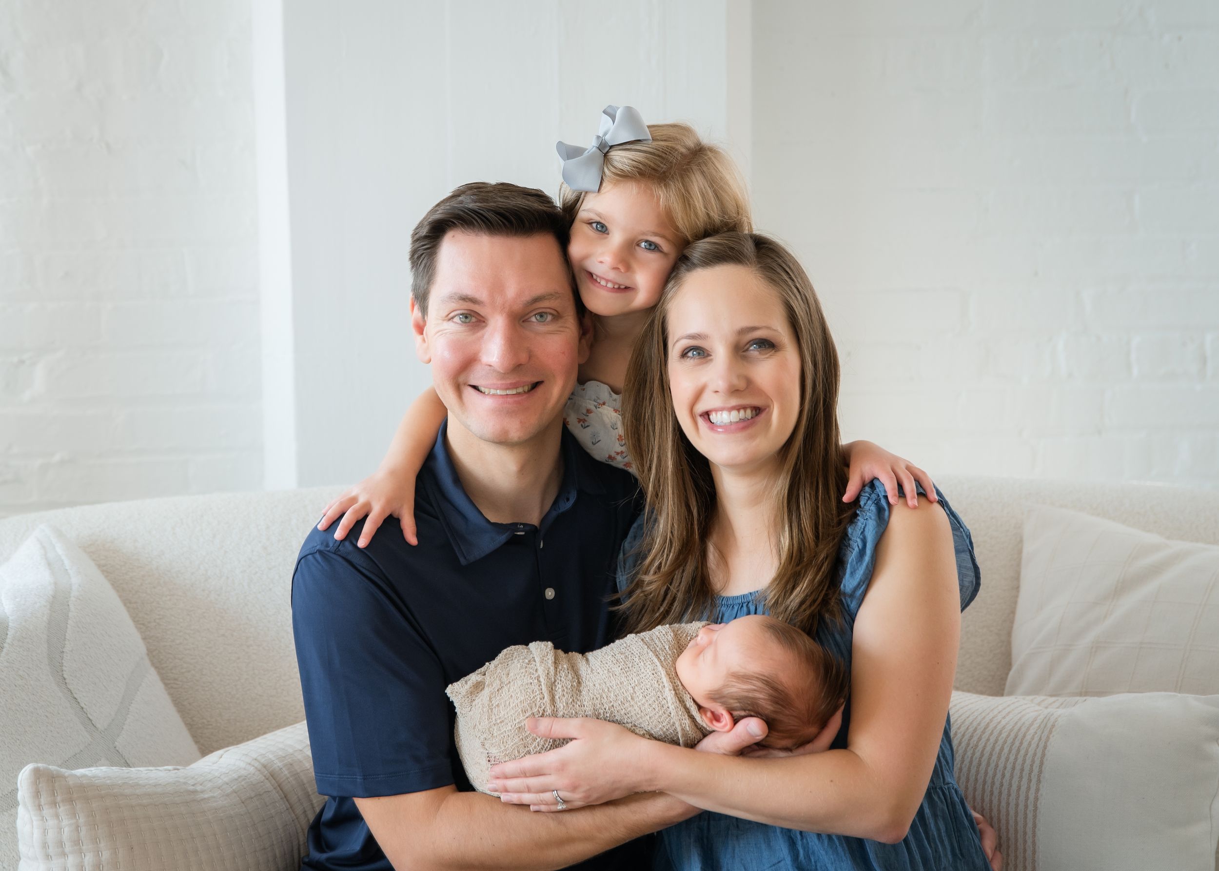 A couple in navy blue outfits sits together on a light gray couch in a bright, modern living room.