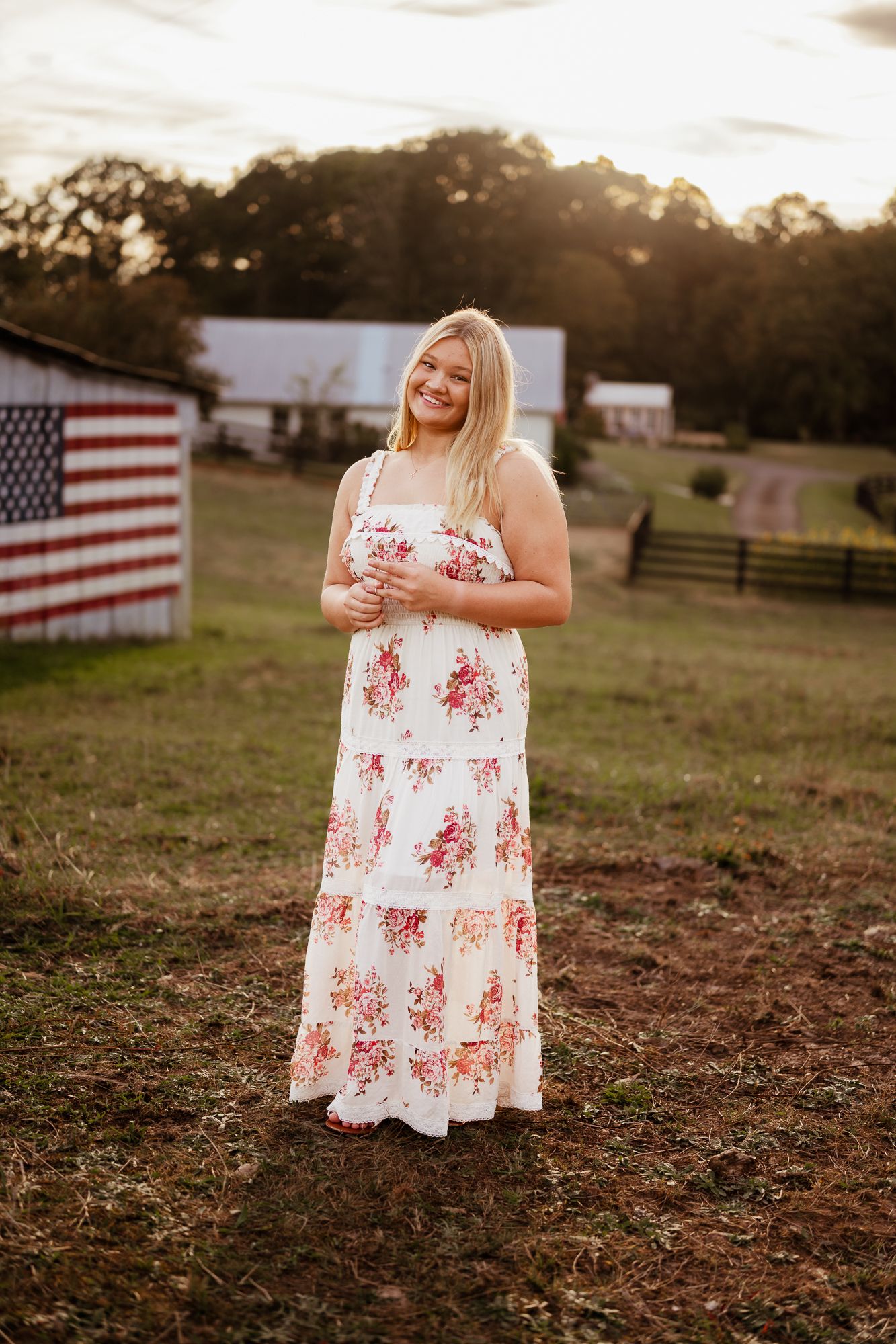 A floral sundress is worn in a rustic outdoor setting with an American flag visible in the background at sunset.
