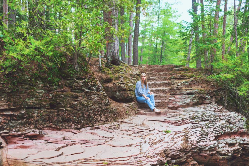A rocky hiking trail winds through a lush green forest in the summertime.