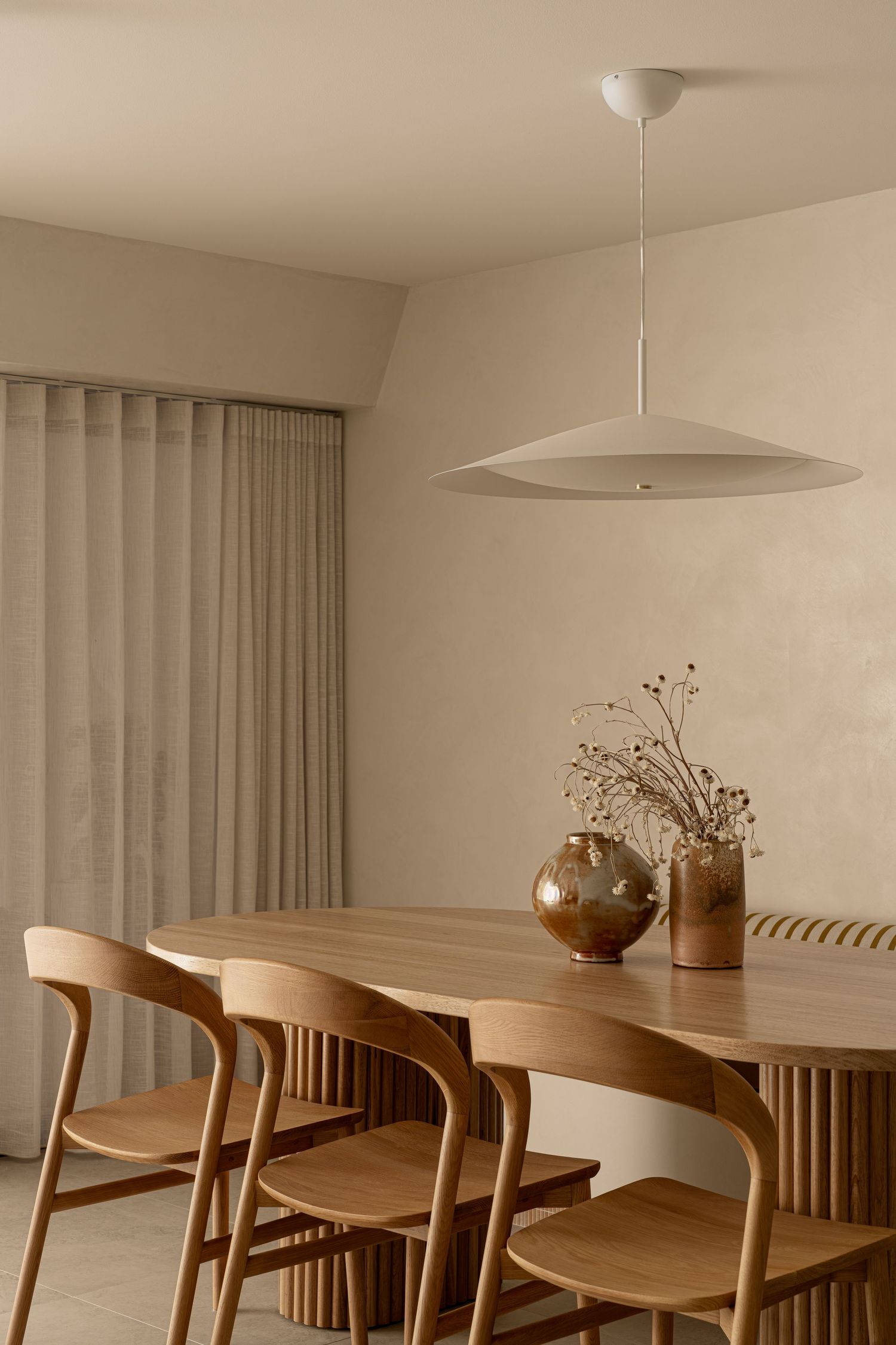 Minimalist dining area with wooden chairs and table beneath a modern pendant light fixture.