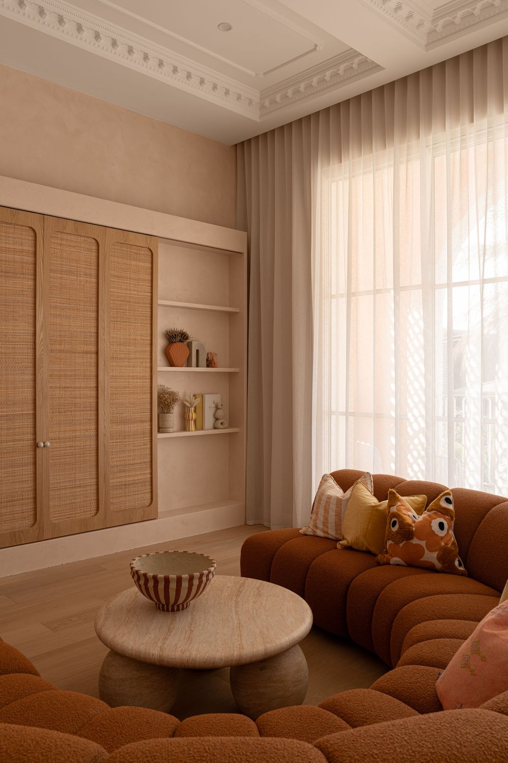 Modern living room with brown sectional sofa, ornate ceiling molding, and natural woven window treatments.