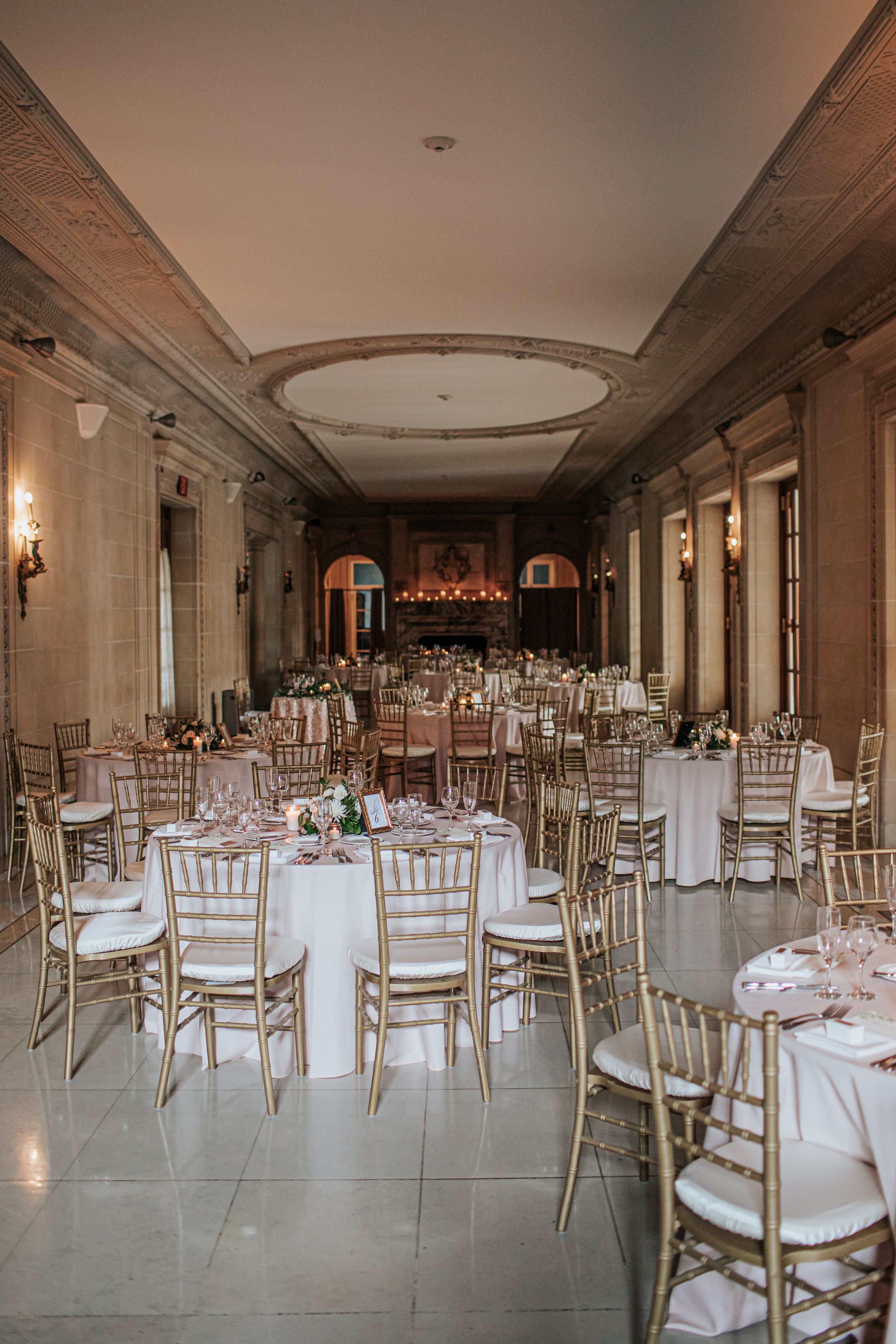 Panoramic view of an elegant wedding reception venue with gold chiavari chairs and white tablecloths set for dining.