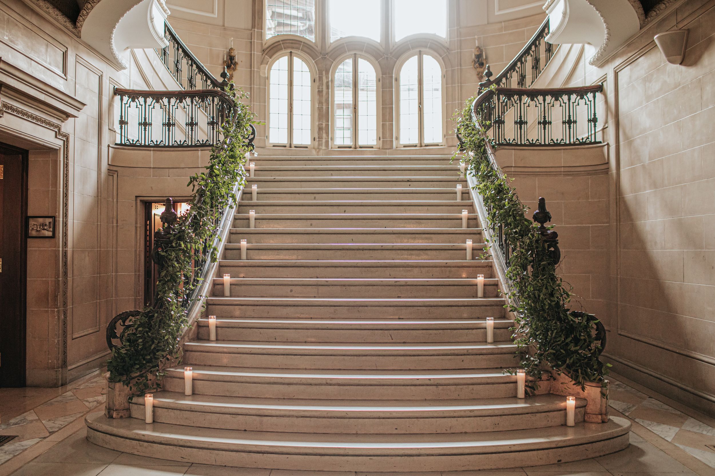 Elegant marble staircase with ornate railings and arched windows in a grand historic building interior.