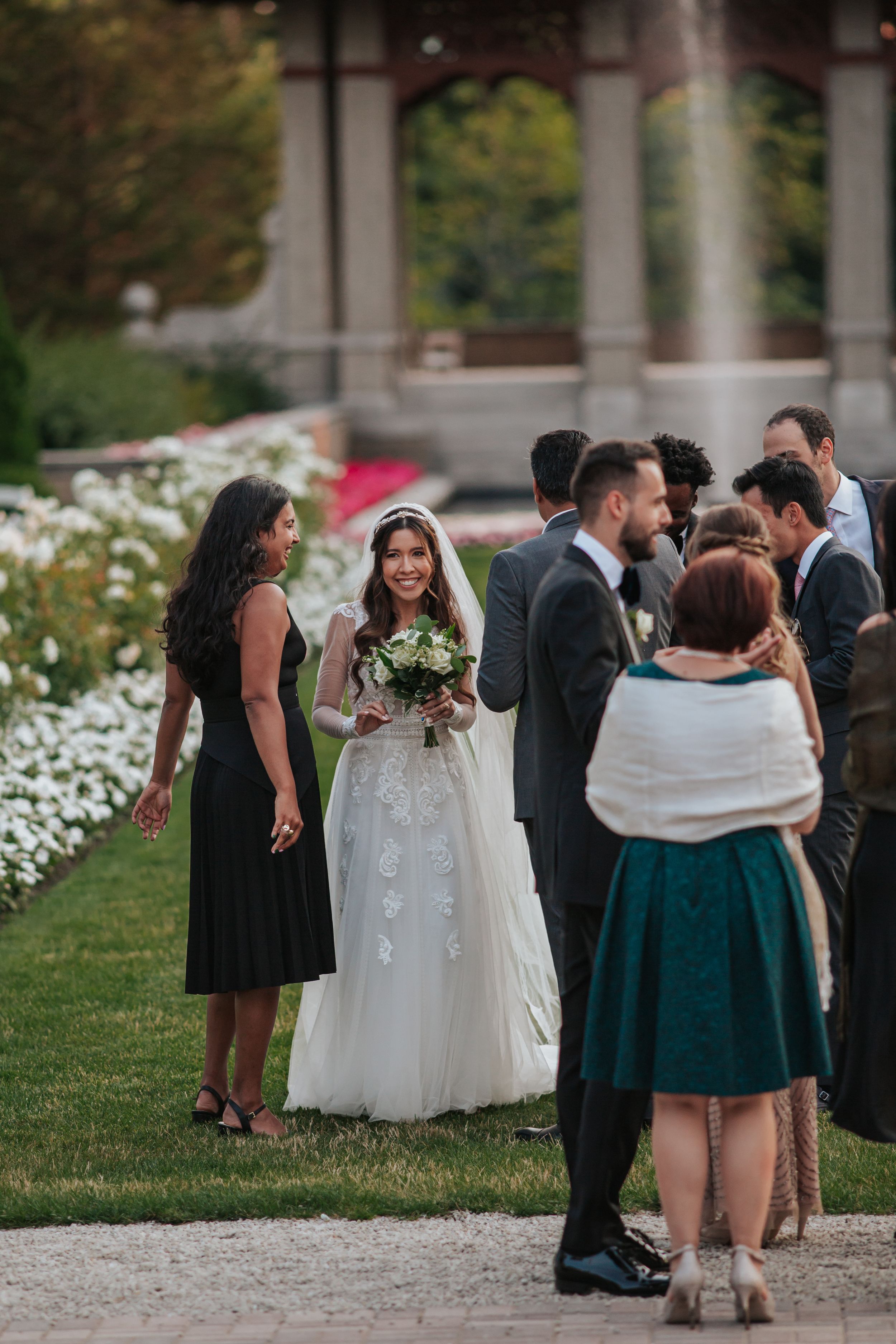 Wedding party members share intimate moments on a grassy lawn with white pillars in the background.