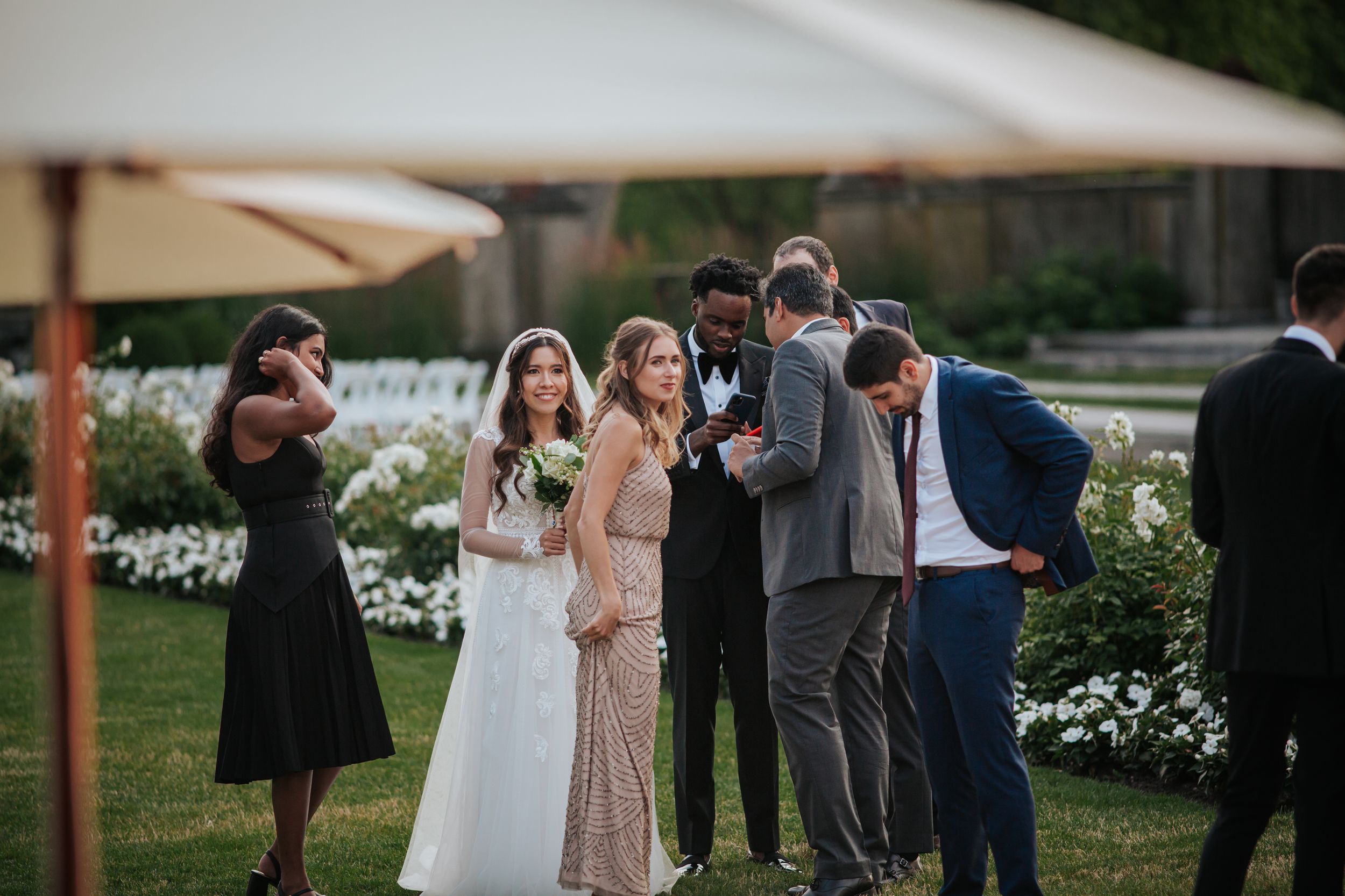 Wedding guests gather outdoors at a reception venue with white tents and string lights at dusk.
