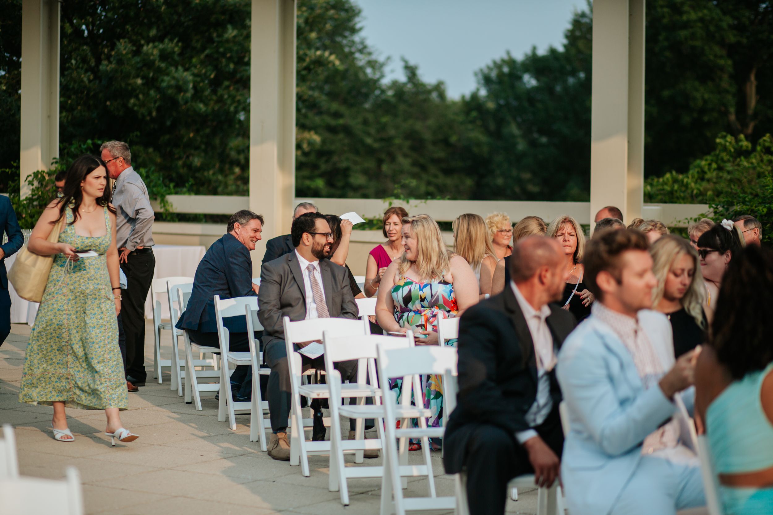 Guests mingle and socialize at an outdoor wedding reception with white chairs and tables set up on a patio.
