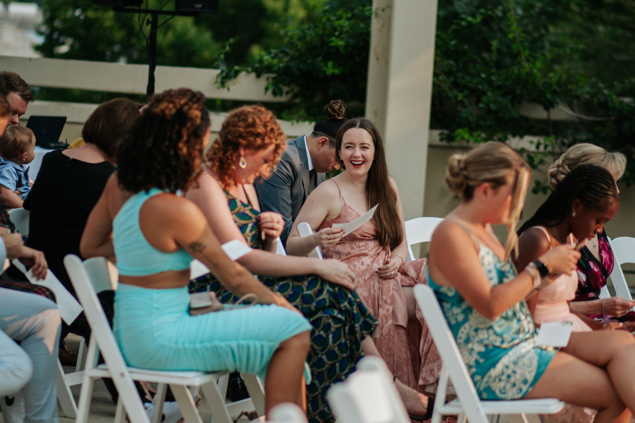 Guests seated at outdoor tables enjoy a casual gathering with food and drinks on a sunny day.